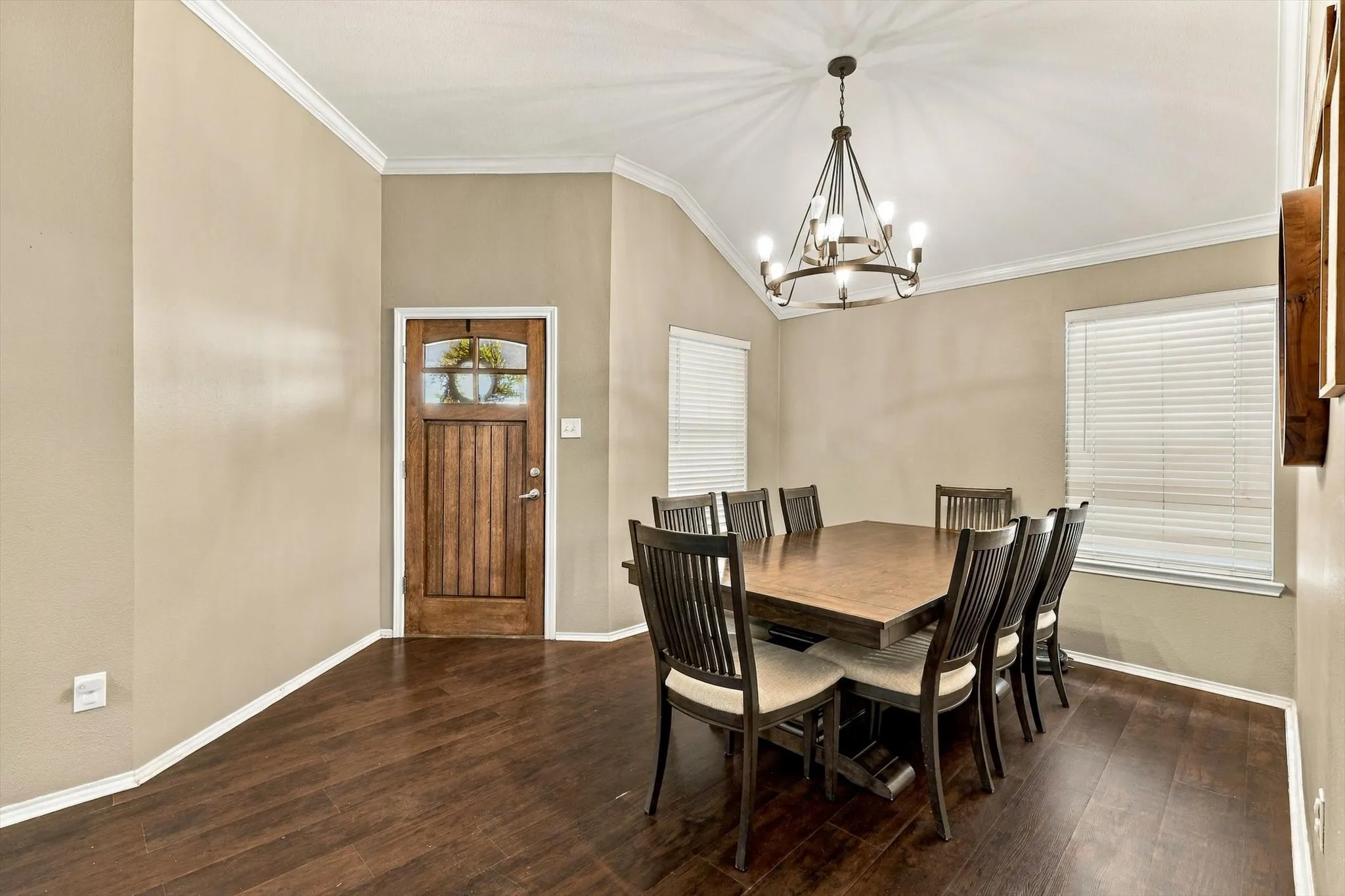 Vaulted ceiling with a chandelier, wood-finish flooring, two windows with blinds, and a wood entry door with glass paneling