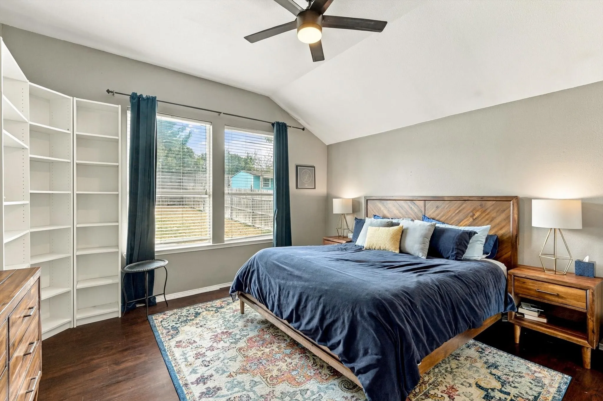 Vaulted ceiling with ceiling fan, wood-finish flooring, two window openings, and built-in shelving