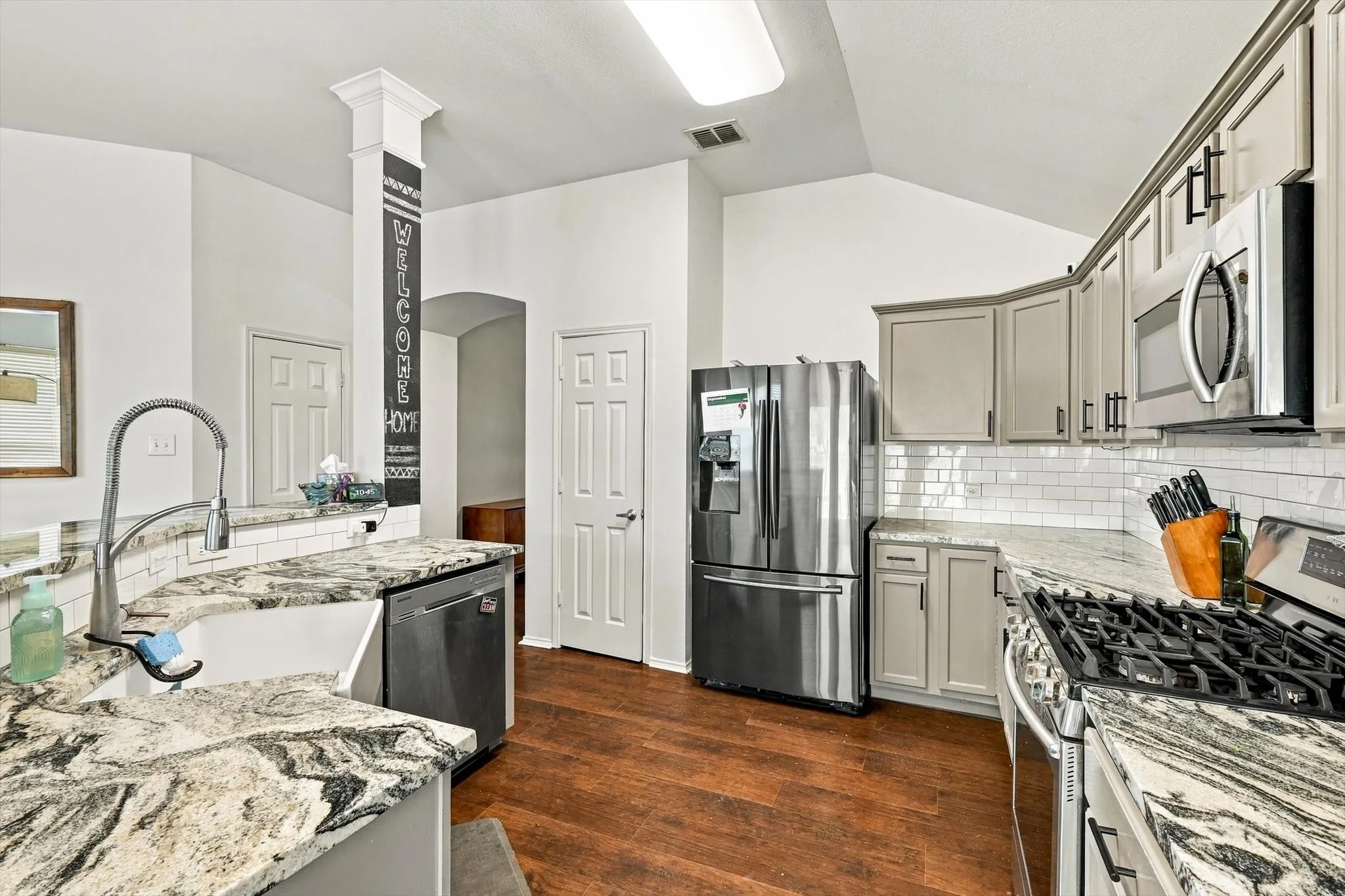 Kitchen featuring wood-finish flooring, stone countertops, white subway tile backsplash, and stainless steel appliances