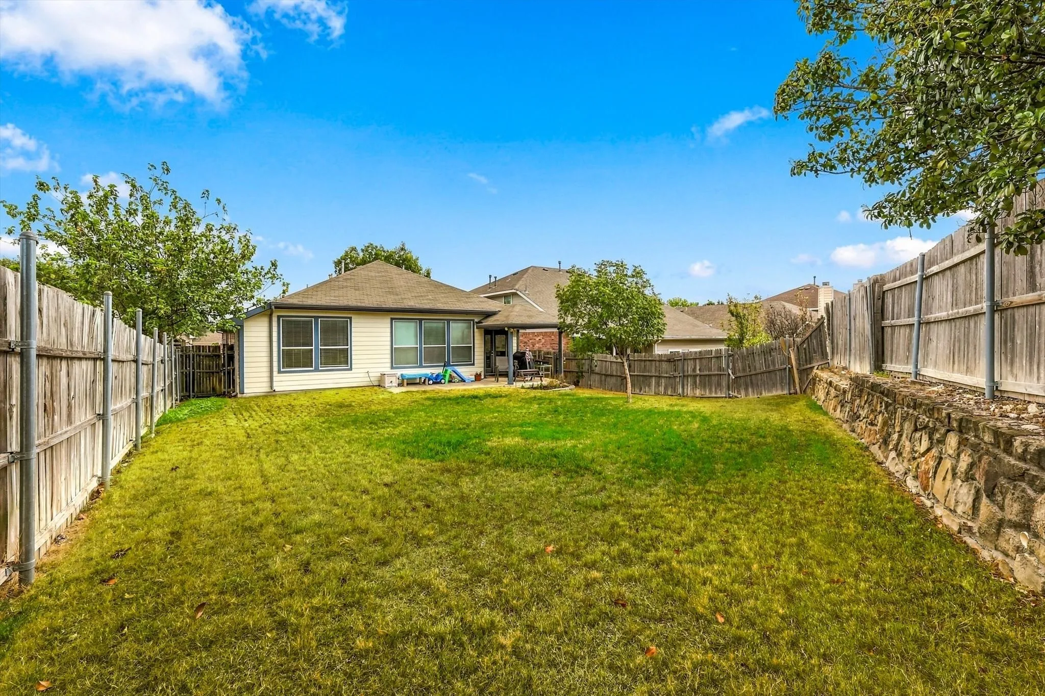 Expansive grassy yard with wood fencing and a stone retaining wall