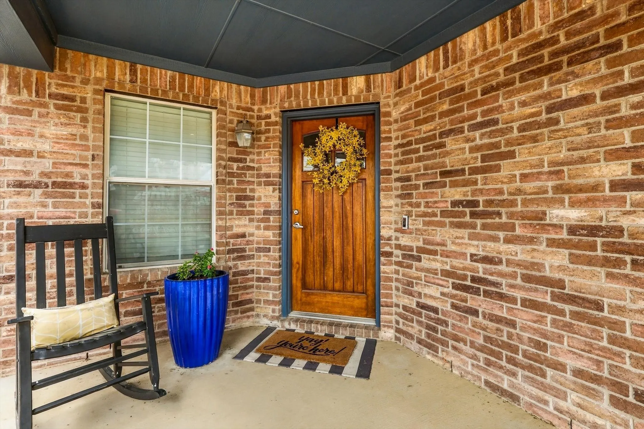 Brick exterior with a covered porch, solid wood entry door, and exterior lighting fixture