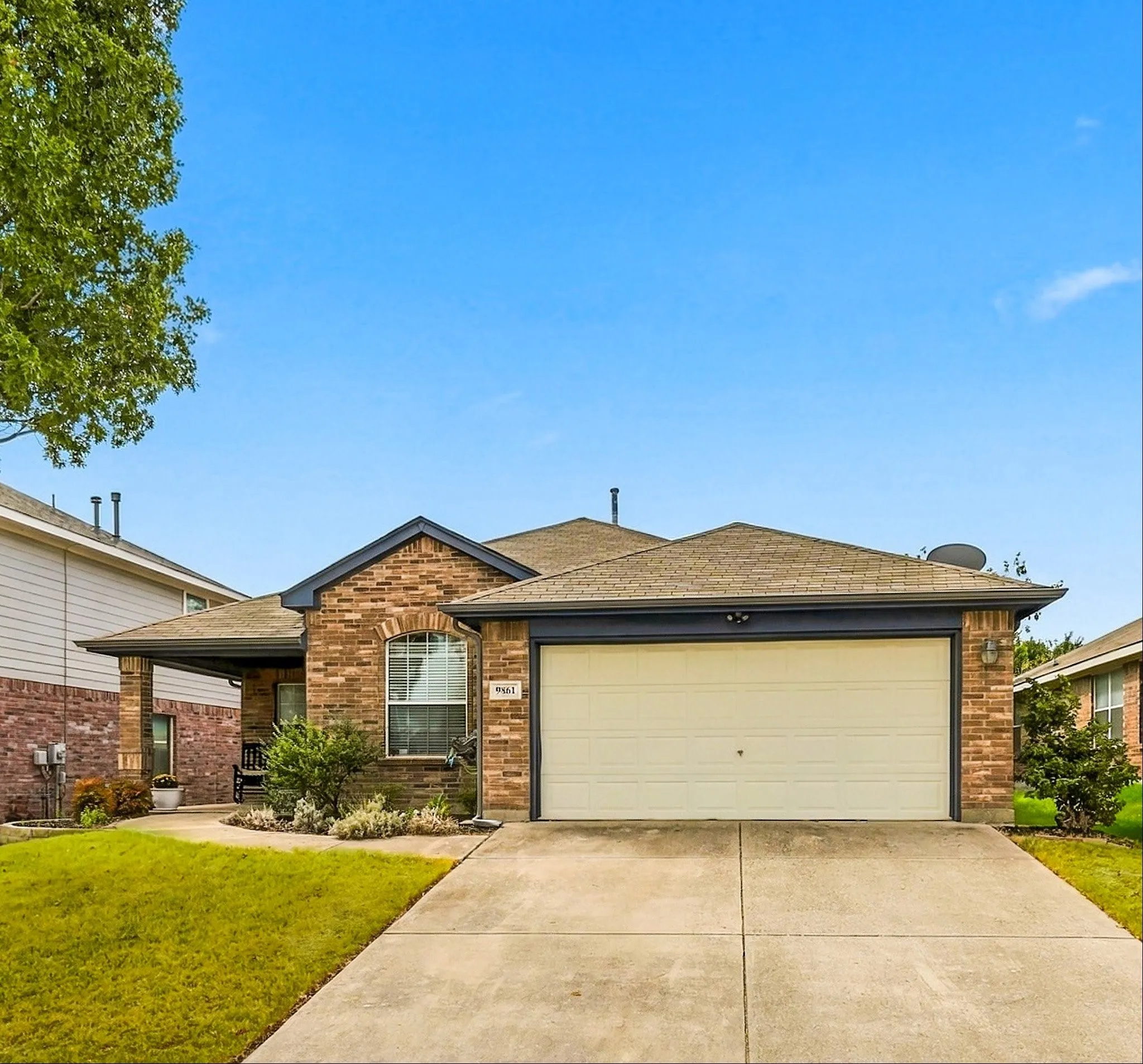 Brick exterior with a covered entry, attached garage, and paved driveway