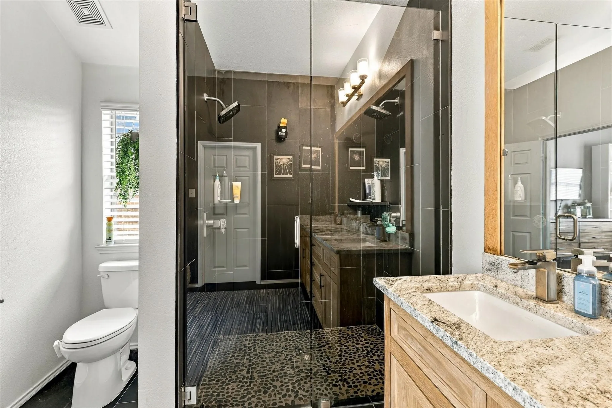 Glass-enclosed shower with pebble-finish flooring and dark-toned wall tile