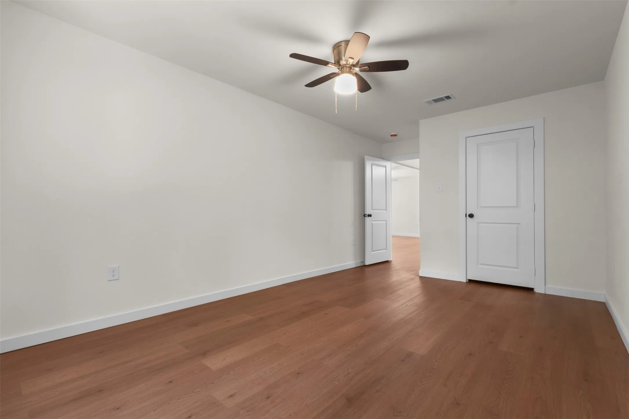 Wood-finish flooring, white walls, white paneled doors, and ceiling fan with integrated lighting