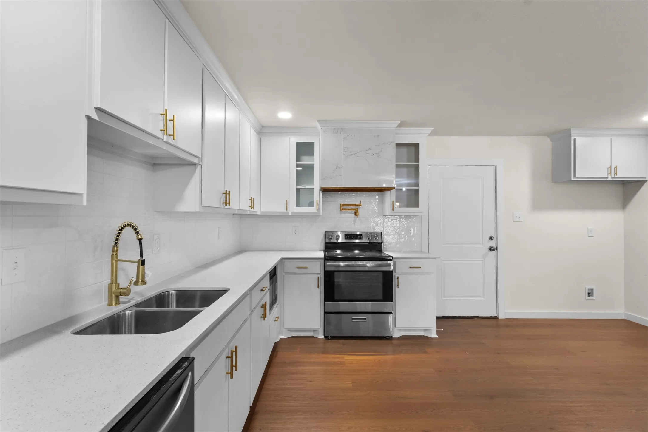White cabinetry with gold-tone hardware, stainless steel appliances, a double basin sink with a gooseneck faucet, light-colored countertops, and wood-finish flooring