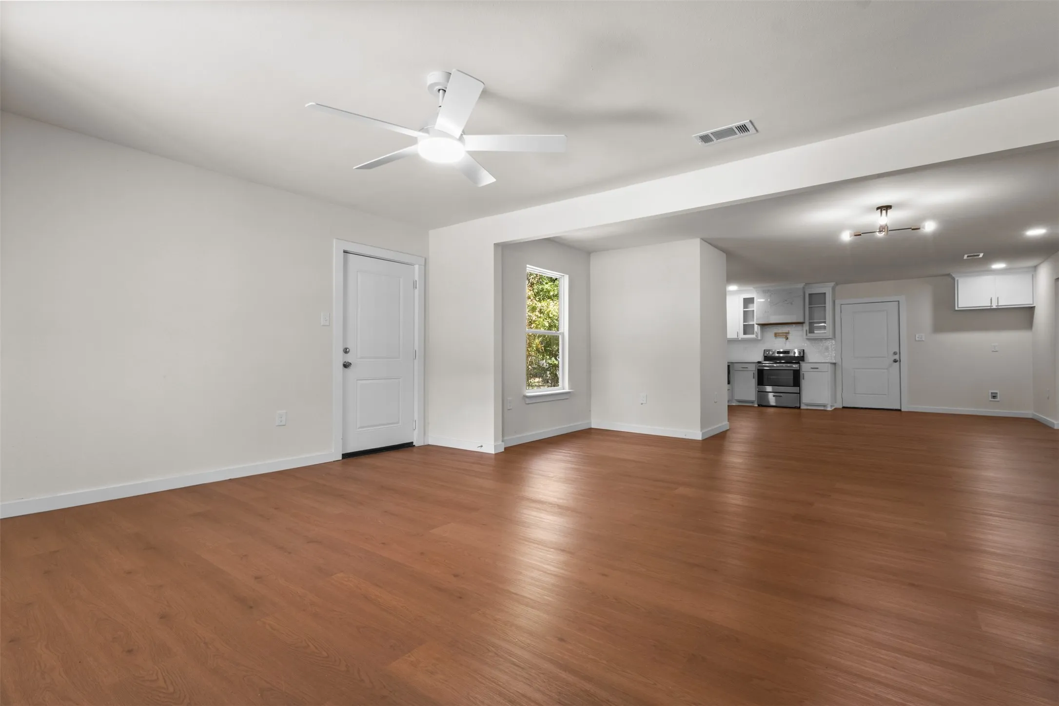 Spacious open-concept living area featuring wood-finish flooring and a contemporary ceiling fan