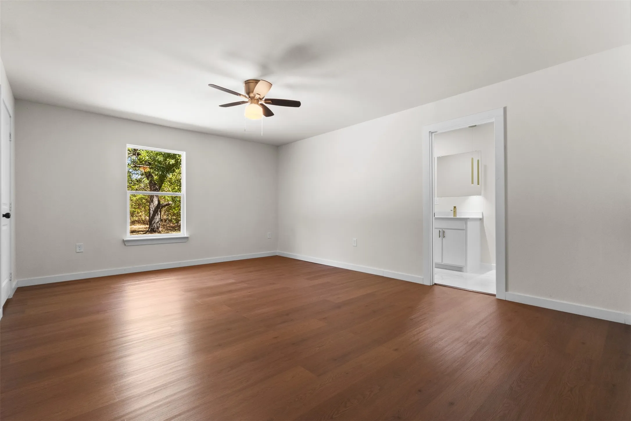 Spacious room featuring wood-finish flooring, a ceiling fan, and a window