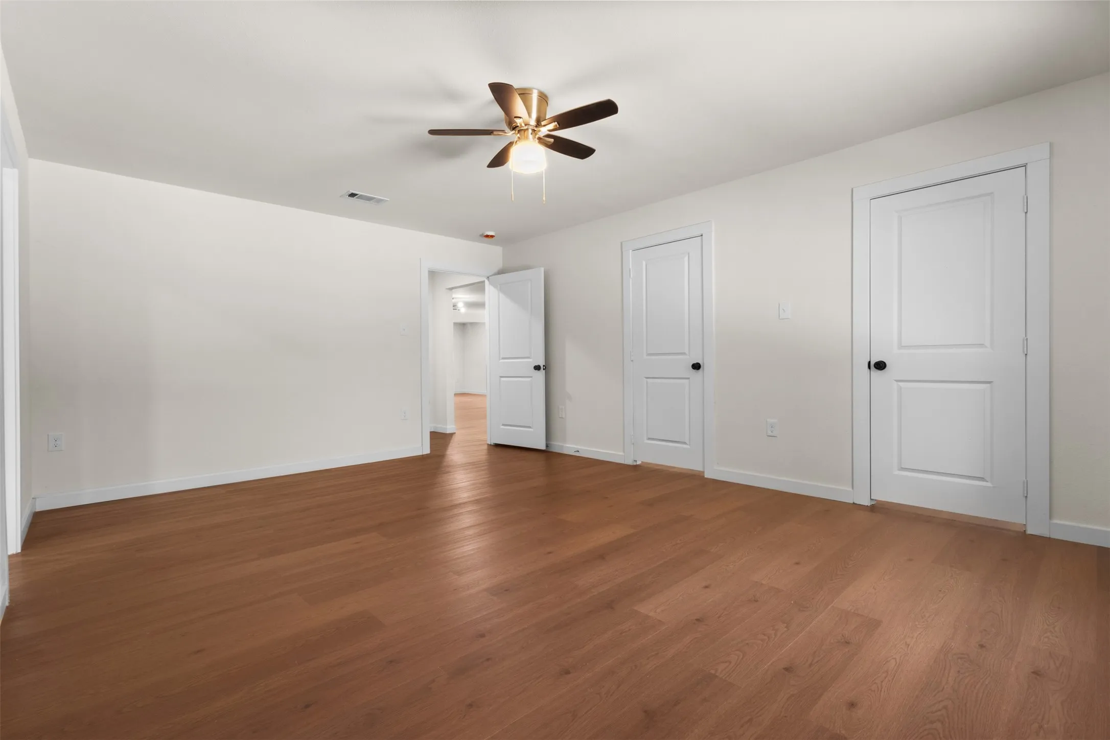Expansive room featuring wood-finish flooring, a ceiling fan, and multiple two-panel doors