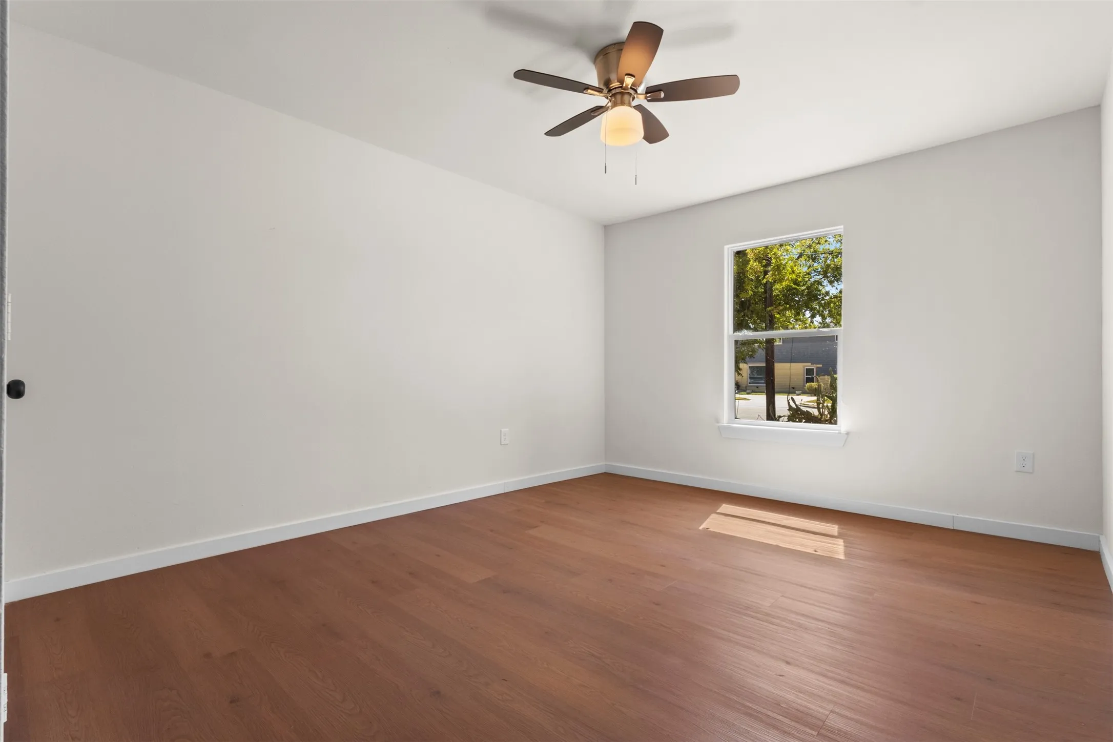Wood-finish flooring with white baseboards, a single window, and a ceiling fan with integrated lighting