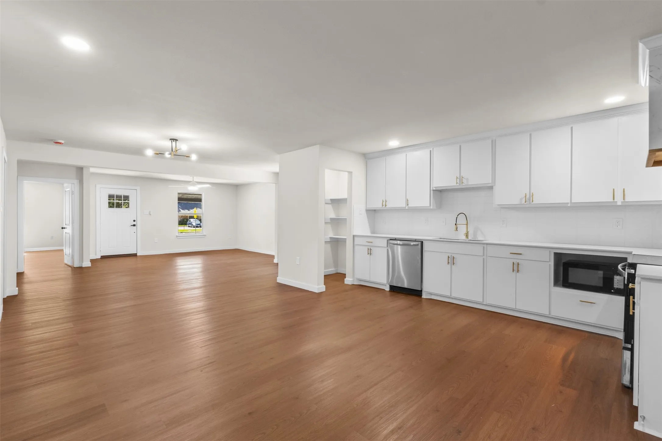 Open-concept kitchen and living area featuring wood-finish flooring, white cabinetry with gold-tone hardware, stainless steel appliances, and recessed lighting