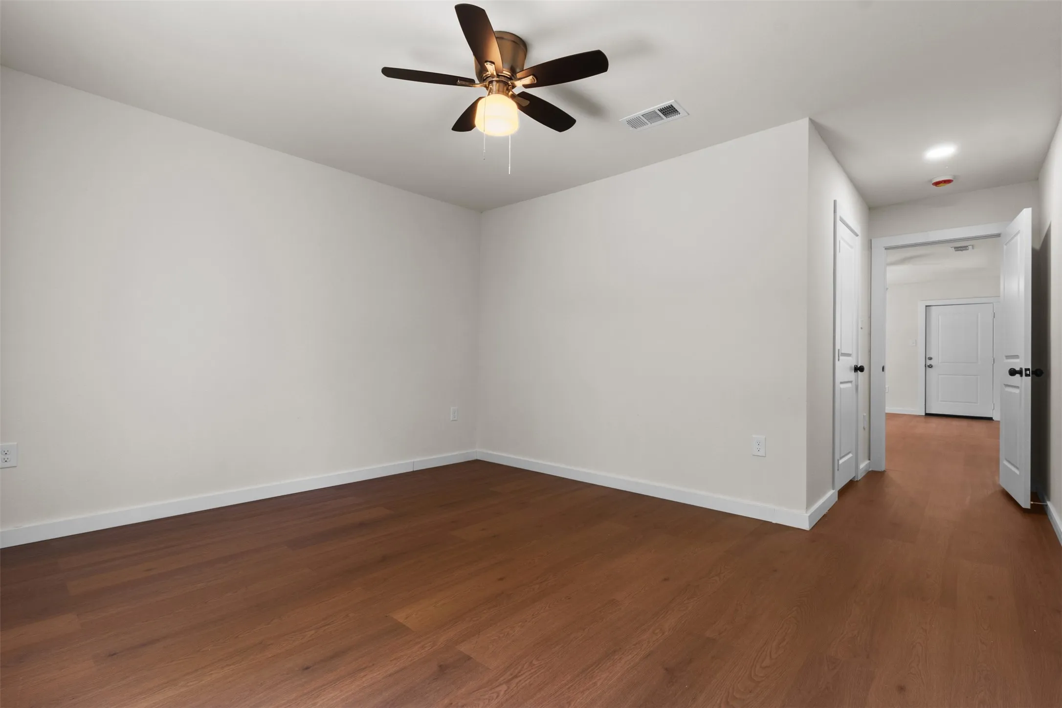 Wood-finish flooring, white walls, and a ceiling fan with integrated lighting