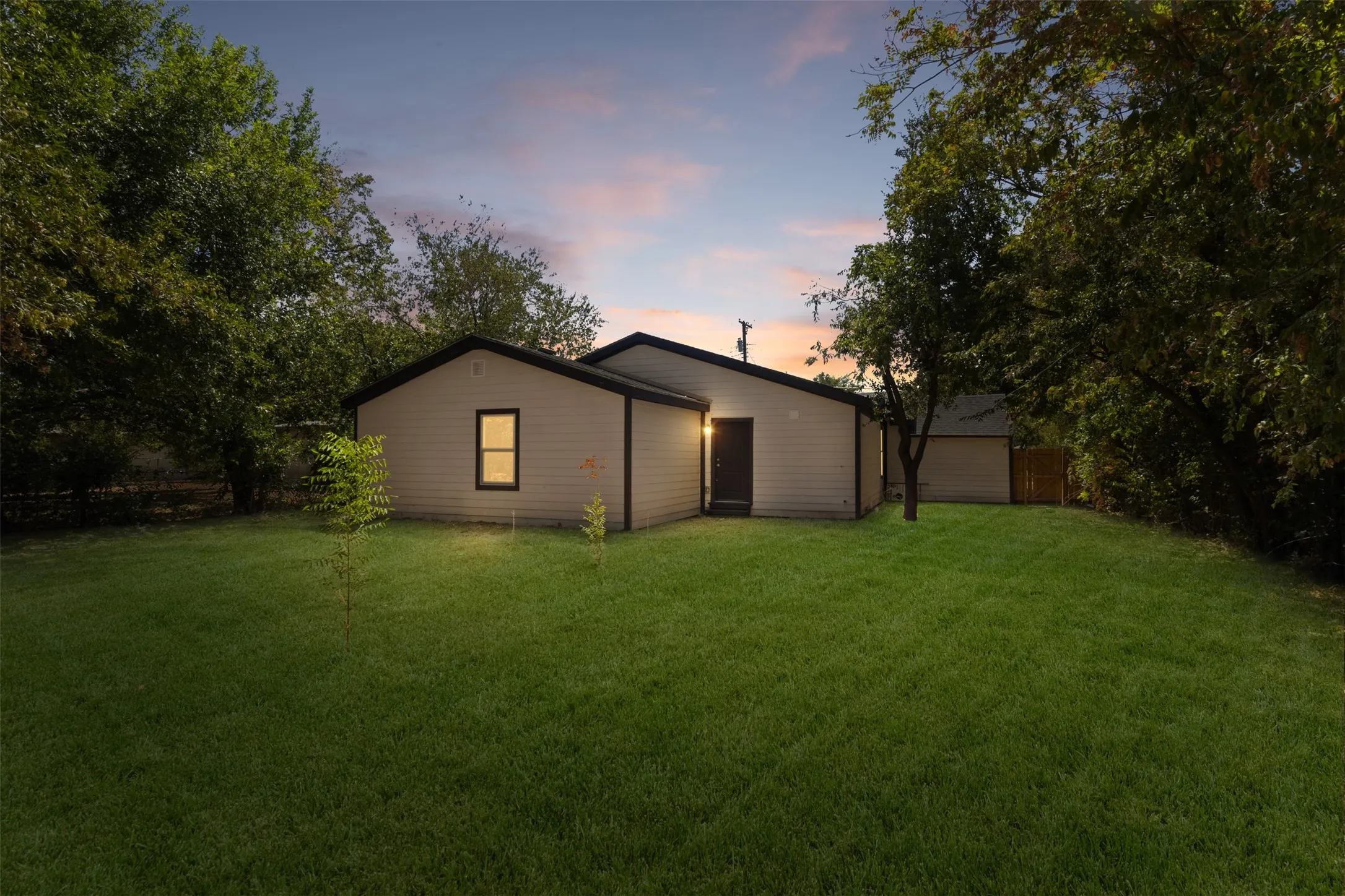 Expansive green lawn with mature trees and a single-story residence featuring light-colored siding and a dark roof