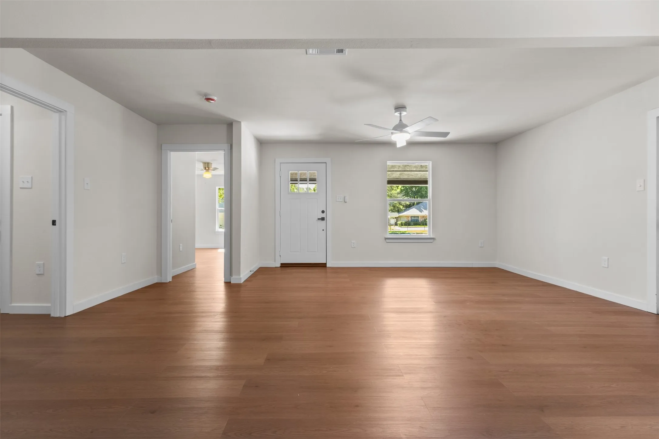Open-concept living area featuring wood-finish flooring, white walls, a ceiling fan, and a window with natural light