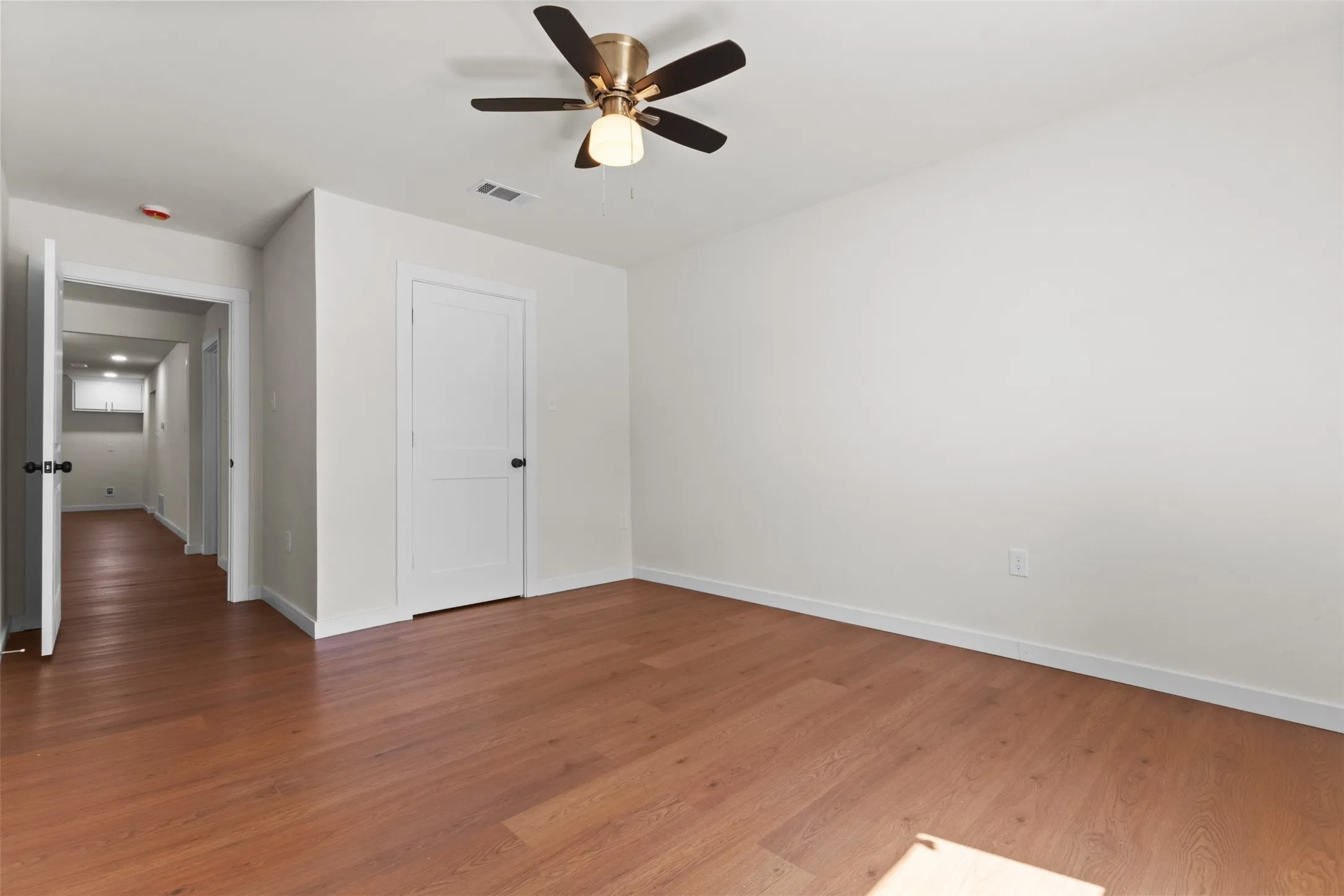 Wood-finish flooring throughout, white walls, and a ceiling fan with integrated lighting