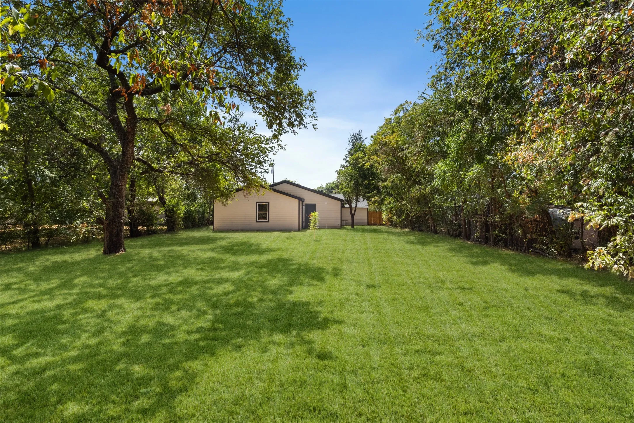 Expansive green lawn with mature trees and a single-story structure with a gabled roof