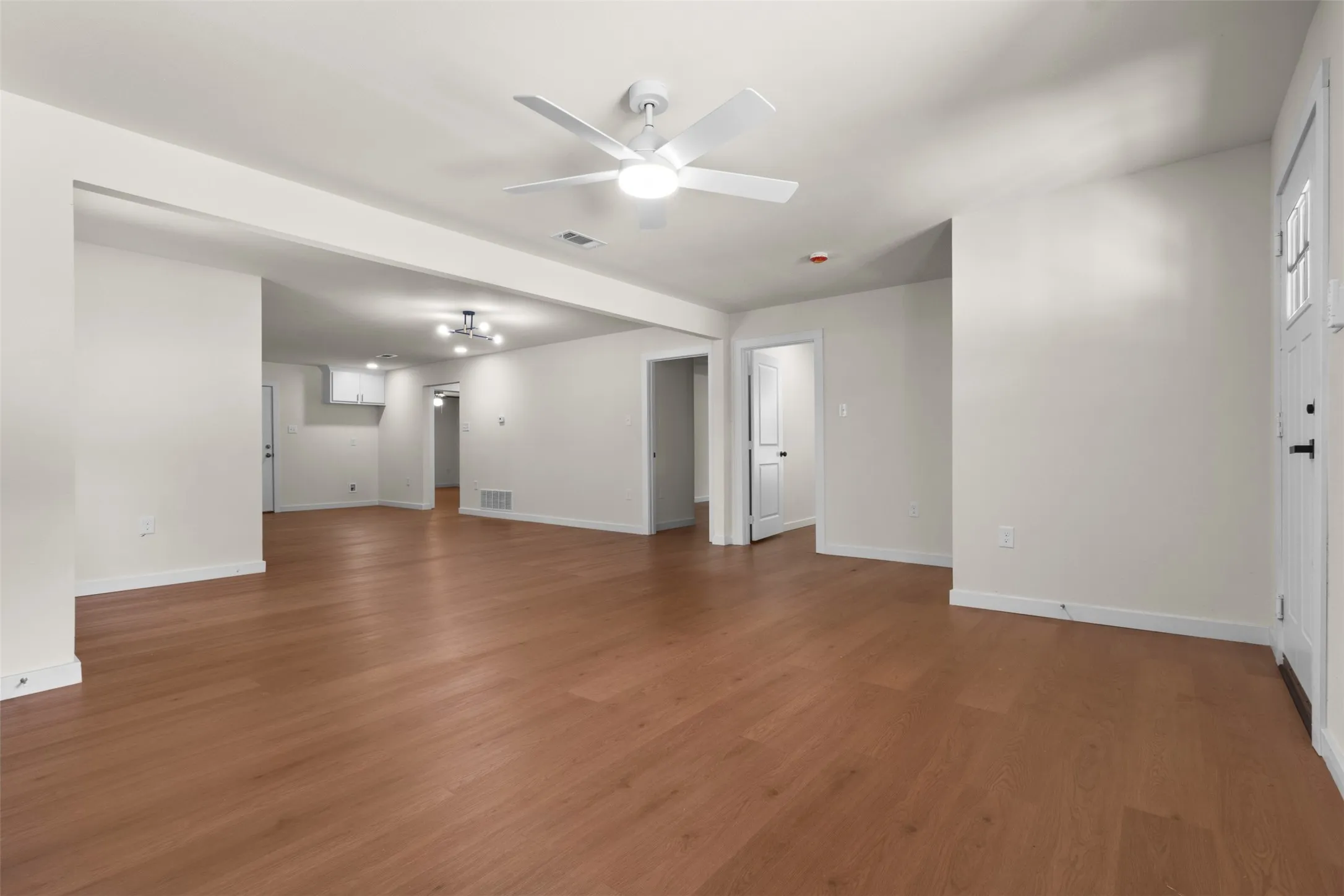 Expansive room featuring wood-finish flooring, white walls, and a ceiling fan with integrated lighting