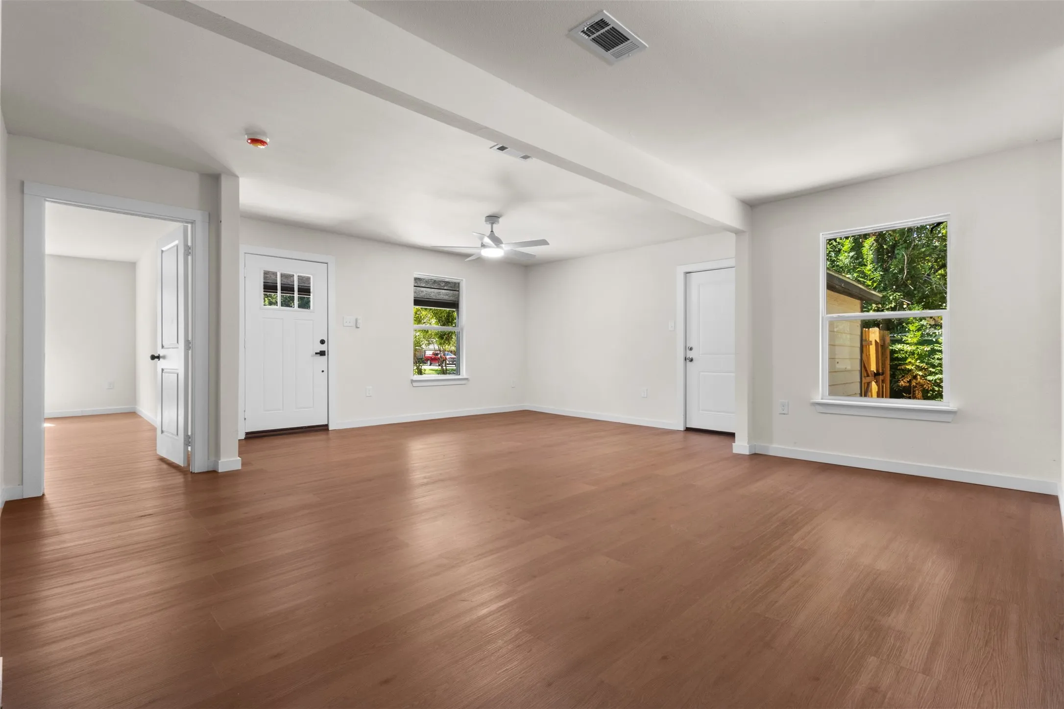 Wood-finish flooring throughout, white interior walls, and a ceiling fan with integrated lighting