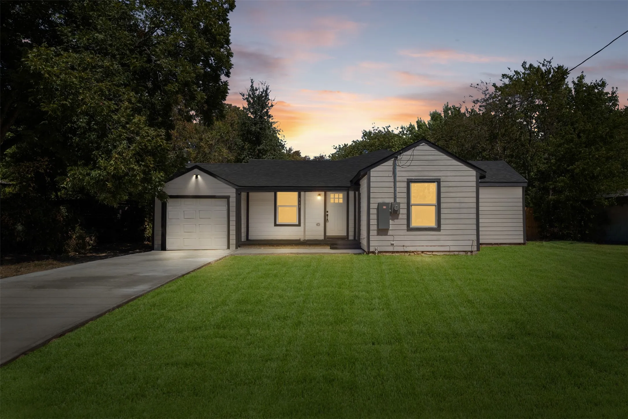 Single-story residence featuring light-colored siding, a dark shingle roof, an attached single-car garage, and a concrete driveway