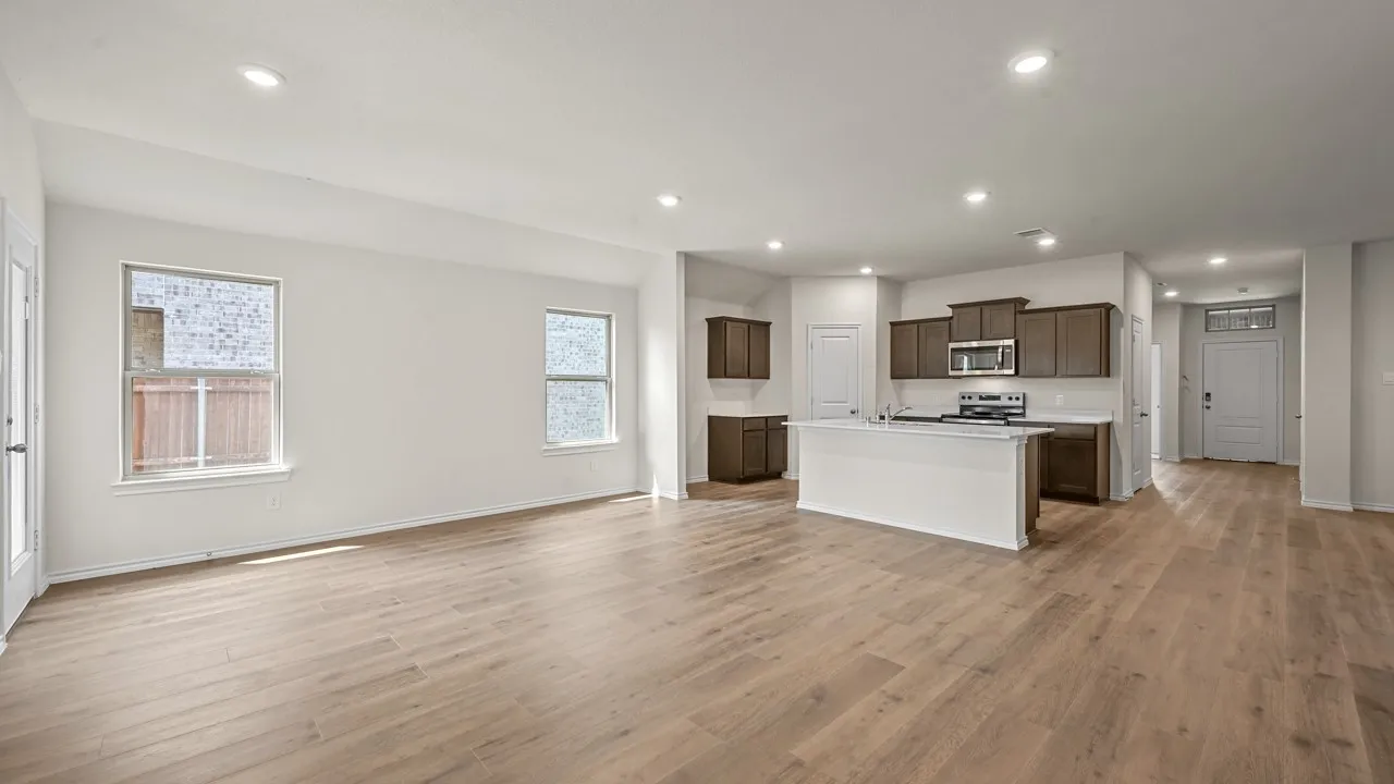 Wood-finish flooring throughout, recessed ceiling lighting, kitchen island with built-in sink, stainless steel appliances, and dark wood-finish cabinetry