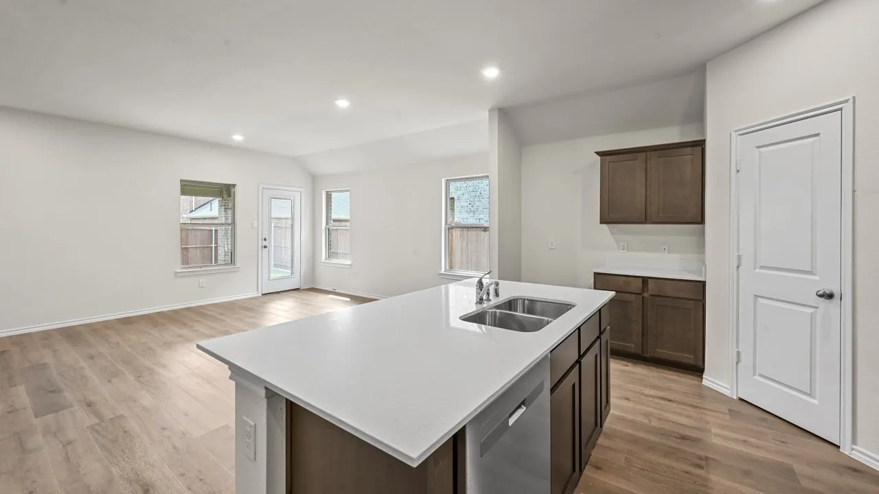 Open-concept kitchen and living area featuring a large island with white quartz countertop and integrated sink, dark wood cabinetry, stainless steel appliances, recessed ceiling lighting, wood-finish flooring throughout, and abundant natural light from multiple windows
