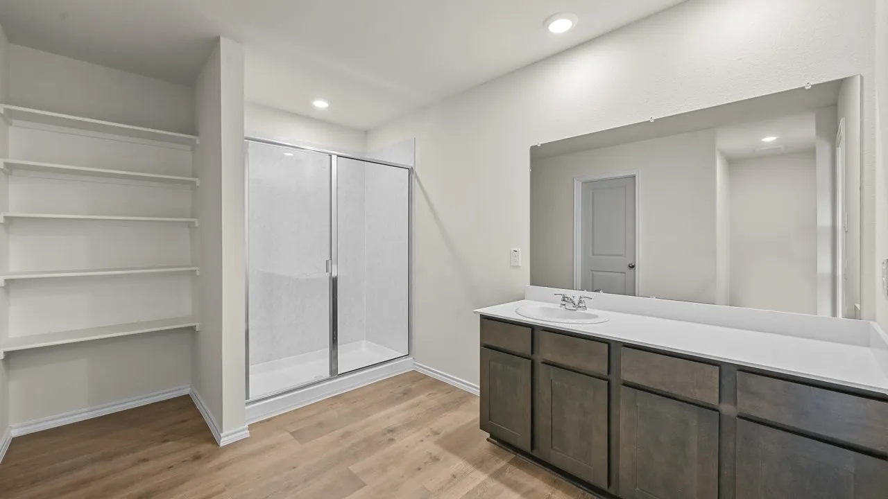 Wood-finish flooring, built-in shelving, glass-enclosed shower, dual-sink vanity, and expansive wall mirror