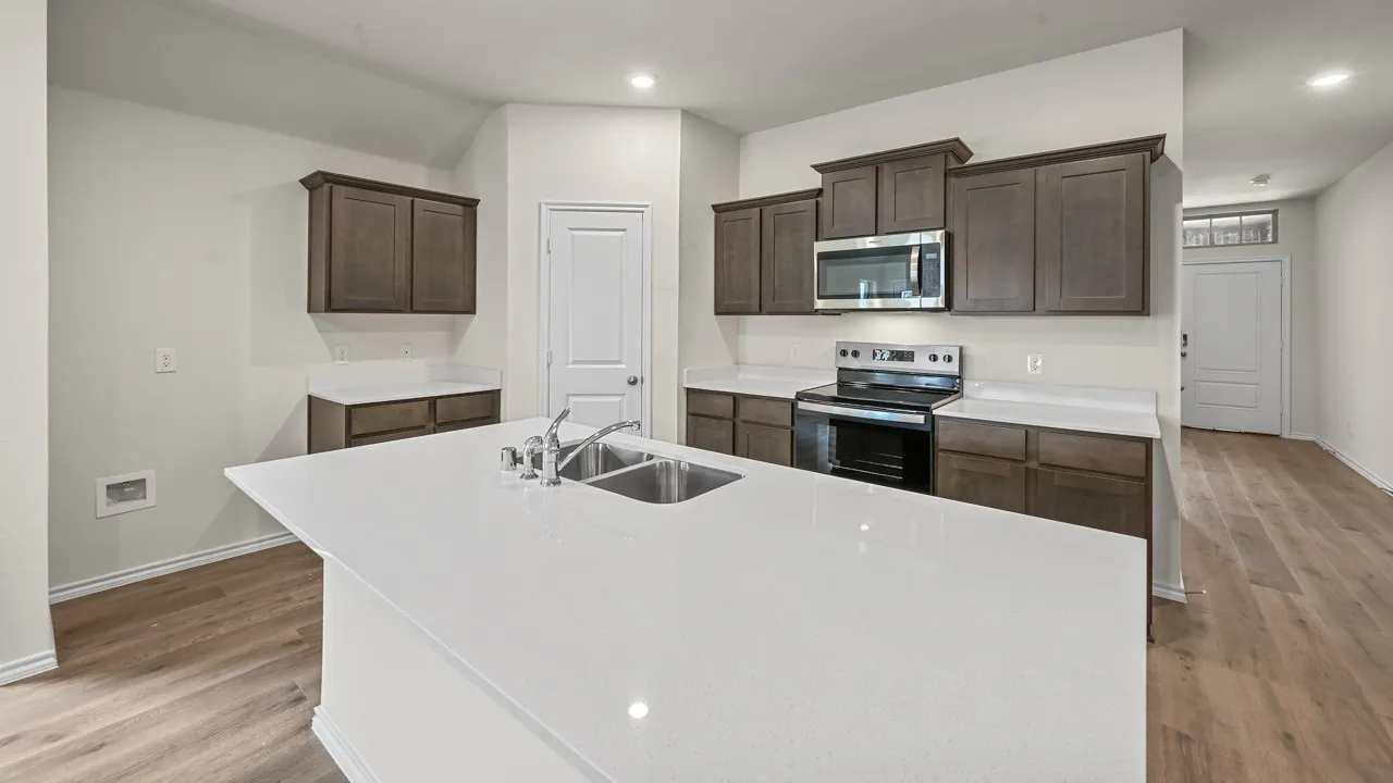 Kitchen featuring a large island with a stainless steel double sink, white countertops, dark wood-finish cabinetry, and wood-finish flooring