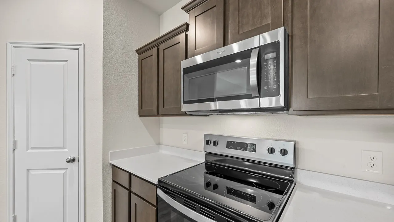 Stainless steel microwave, coordinating stainless steel electric range, white countertops, and wood-finish cabinetry