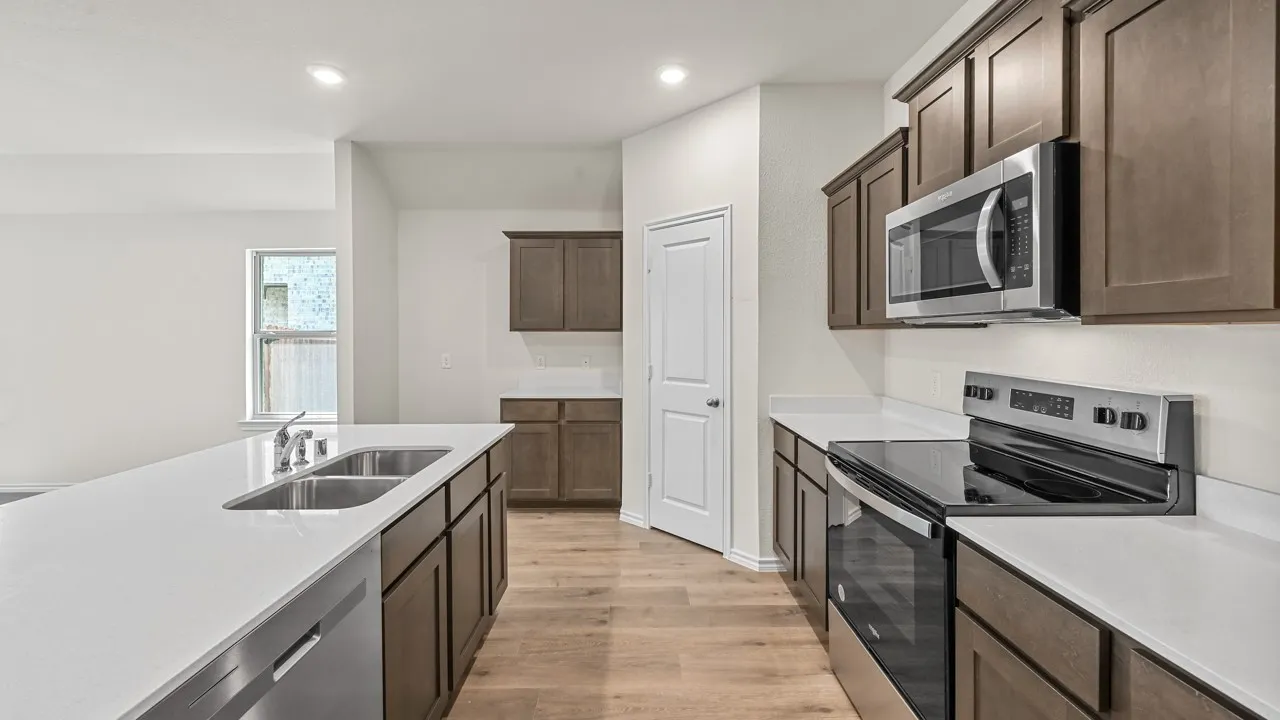 Kitchen featuring wood-finish flooring, stainless steel appliances, white countertops, and dark wood cabinetry