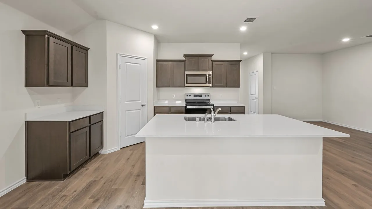 Open-concept kitchen featuring an island with a stainless steel sink, wood-finish flooring, dark wood cabinetry, and stainless steel appliances