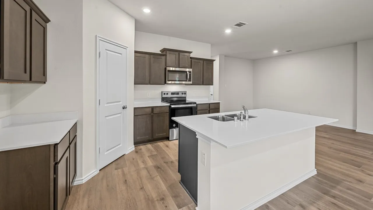 Kitchen featuring dark wood-finish cabinetry, light countertops, a kitchen island with an undermount dual-basin sink, stainless steel appliances, and recessed lighting