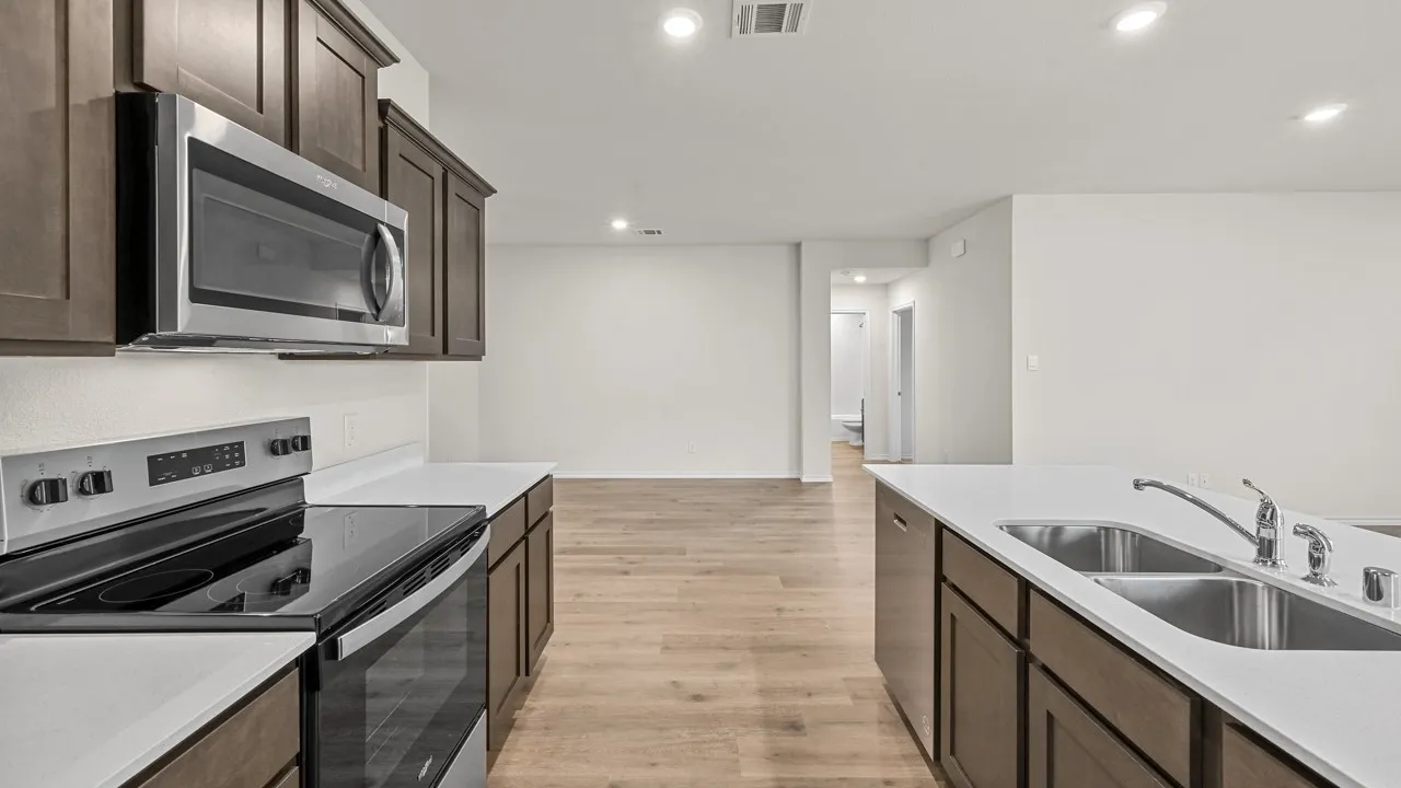 Contemporary kitchen featuring stainless steel appliances, dark wood cabinetry, white countertops, a double basin sink, and wood-finish flooring