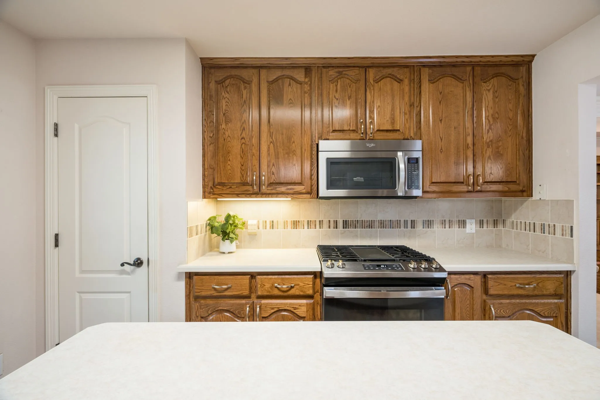 Wood cabinetry with crown molding, stainless steel microwave, gas range, tile backsplash, and solid surface countertops