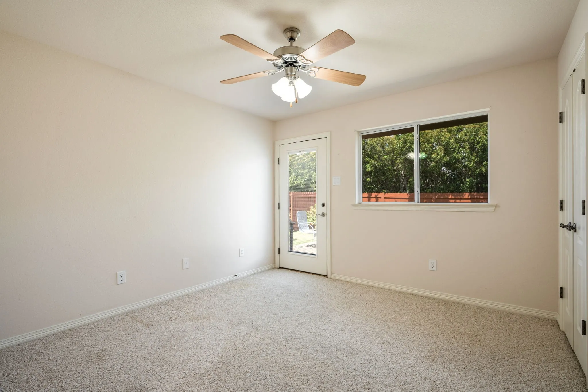 Neutral tone carpeting, ceiling fan with light fixture, white trim, glass-paned door, and large window