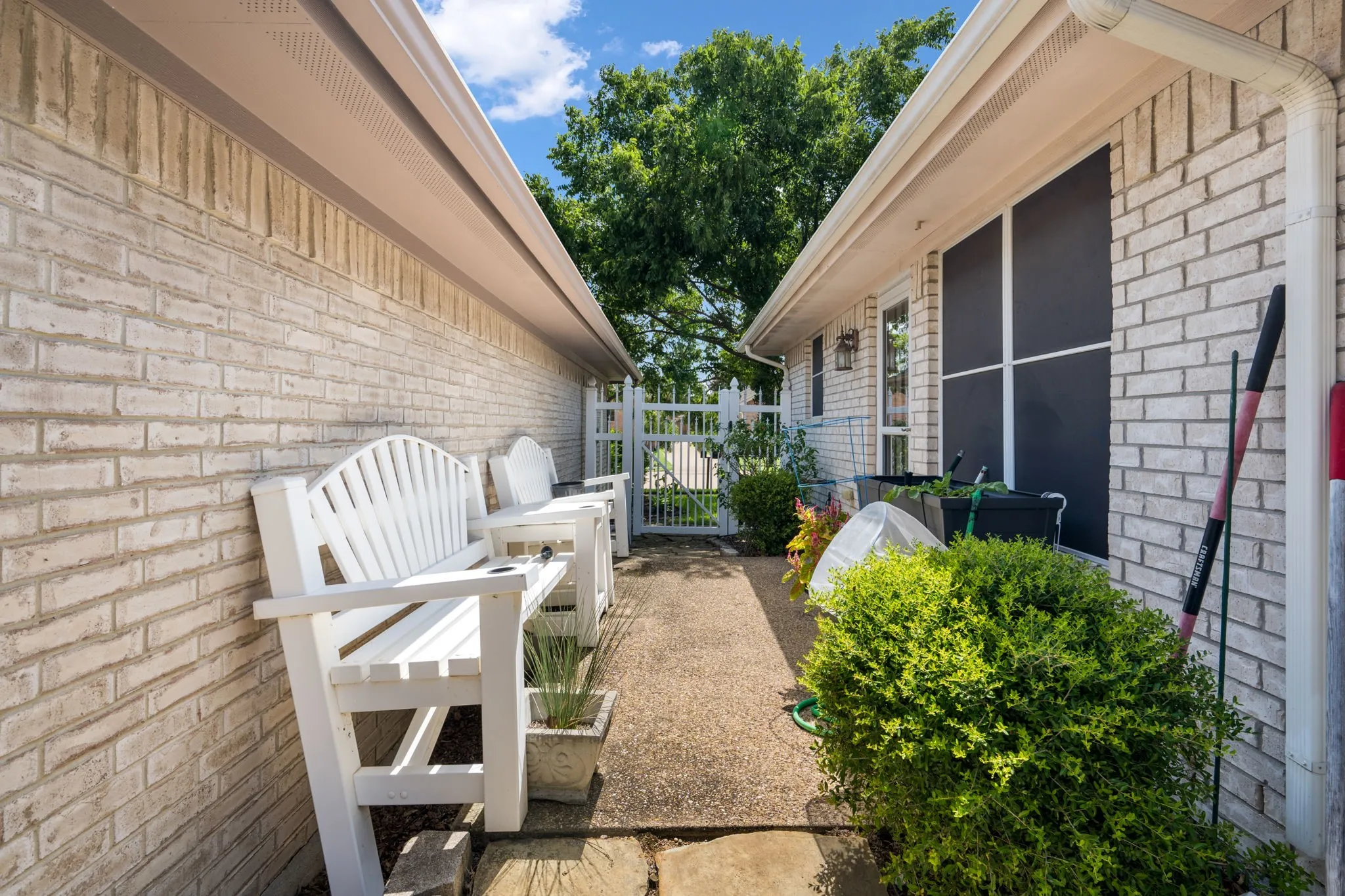 Brick exterior with white soffit and fascia, featuring a concrete pathway and a white privacy gate