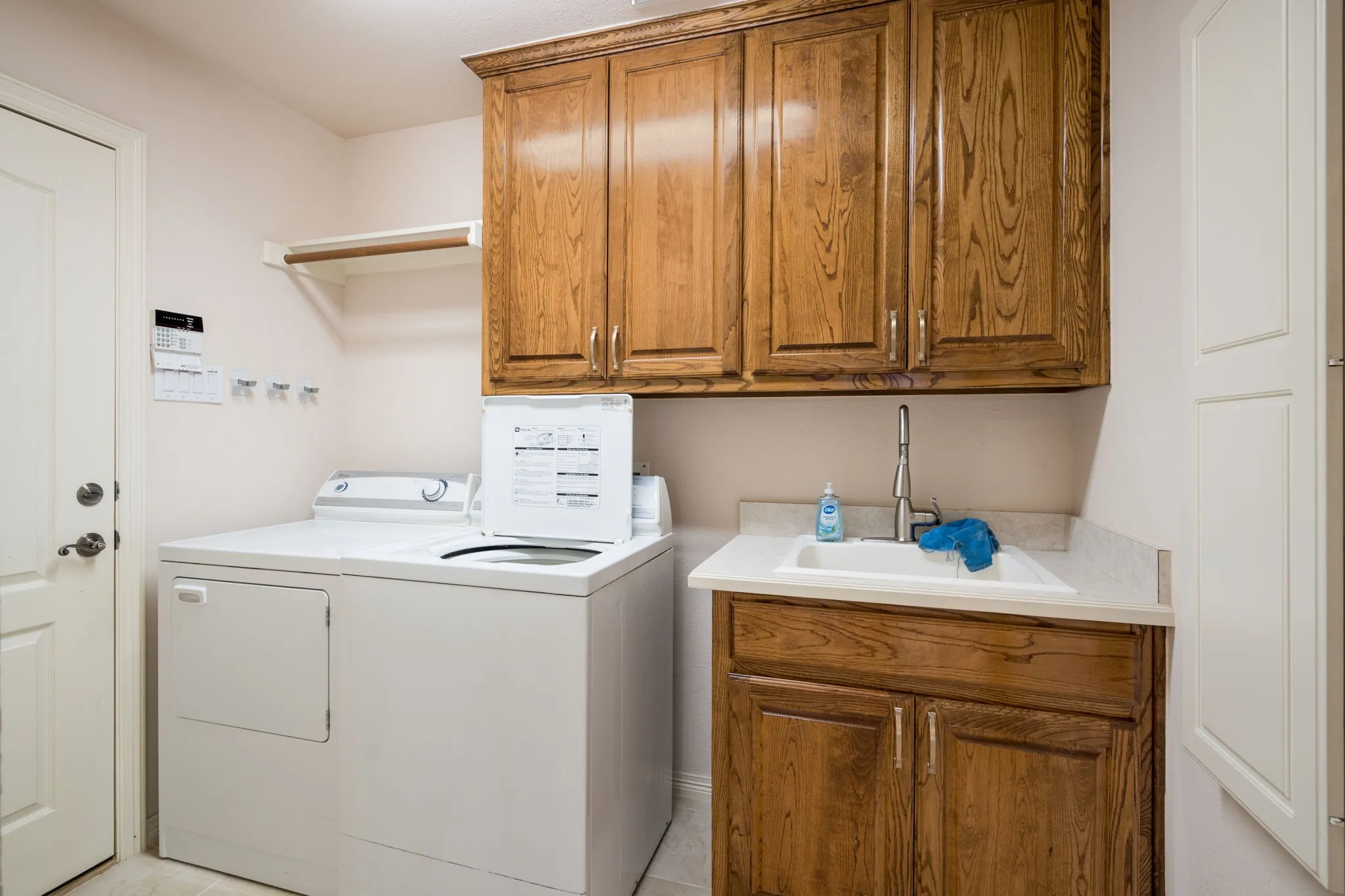 Utility room featuring a built-in sink with a high-arc faucet, wood-finish cabinetry, upper storage, and a clothes hanging rod