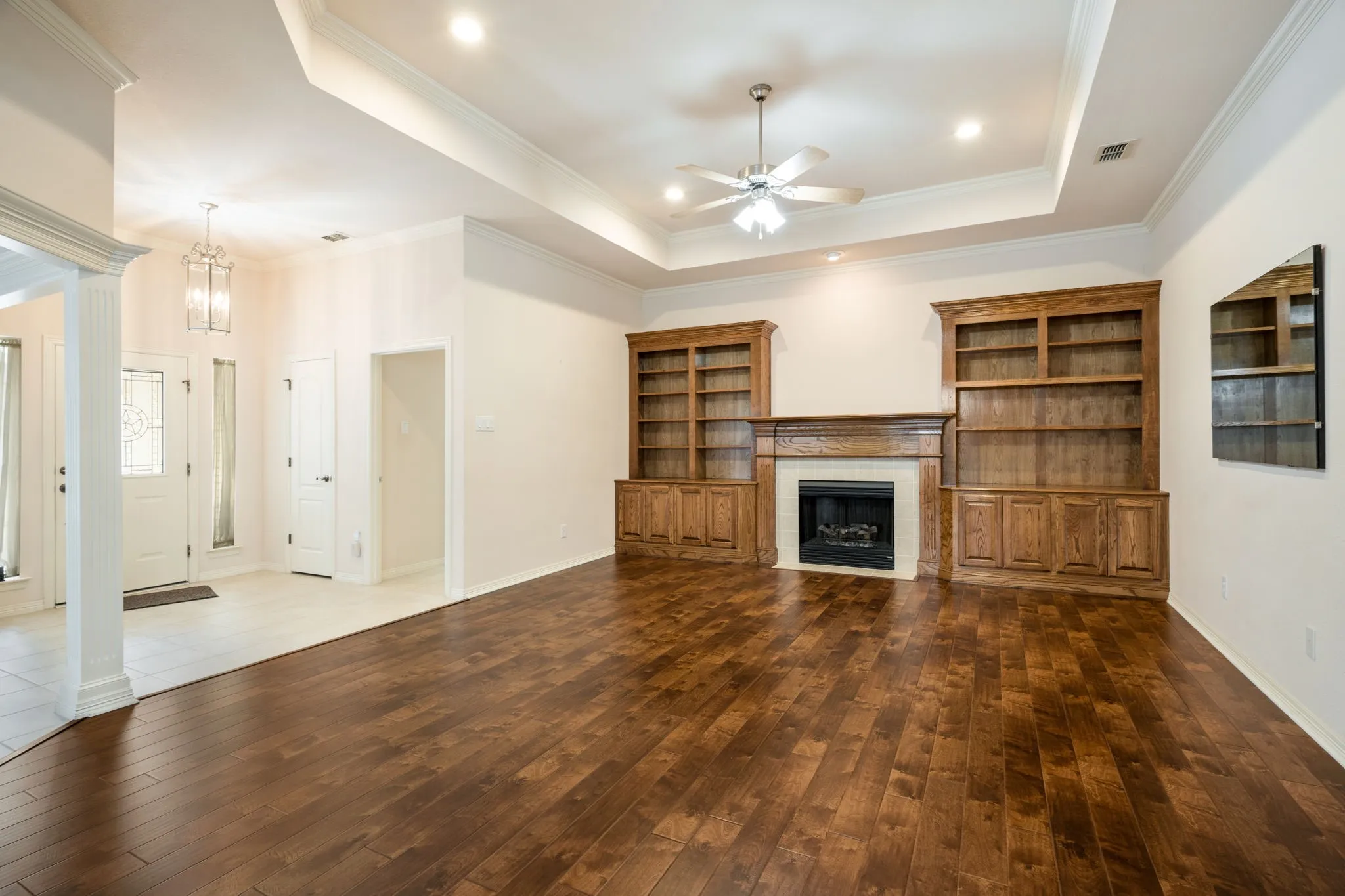 Wood-finish flooring, recessed lighting, ceiling fan, built-in shelving, and a fireplace with a mantel