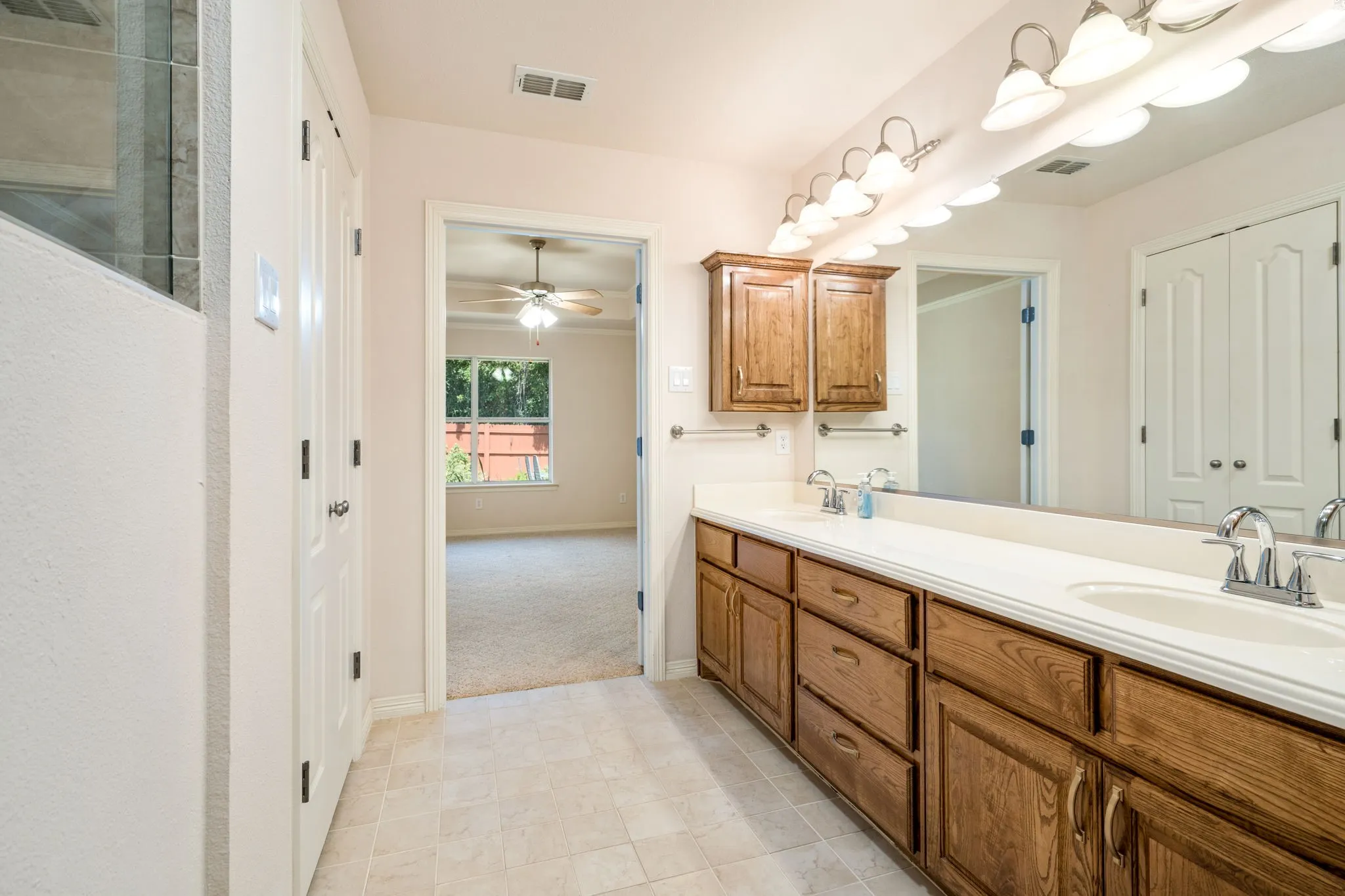 Dual vanity with wood-finish cabinetry, white countertops, and integrated sinks