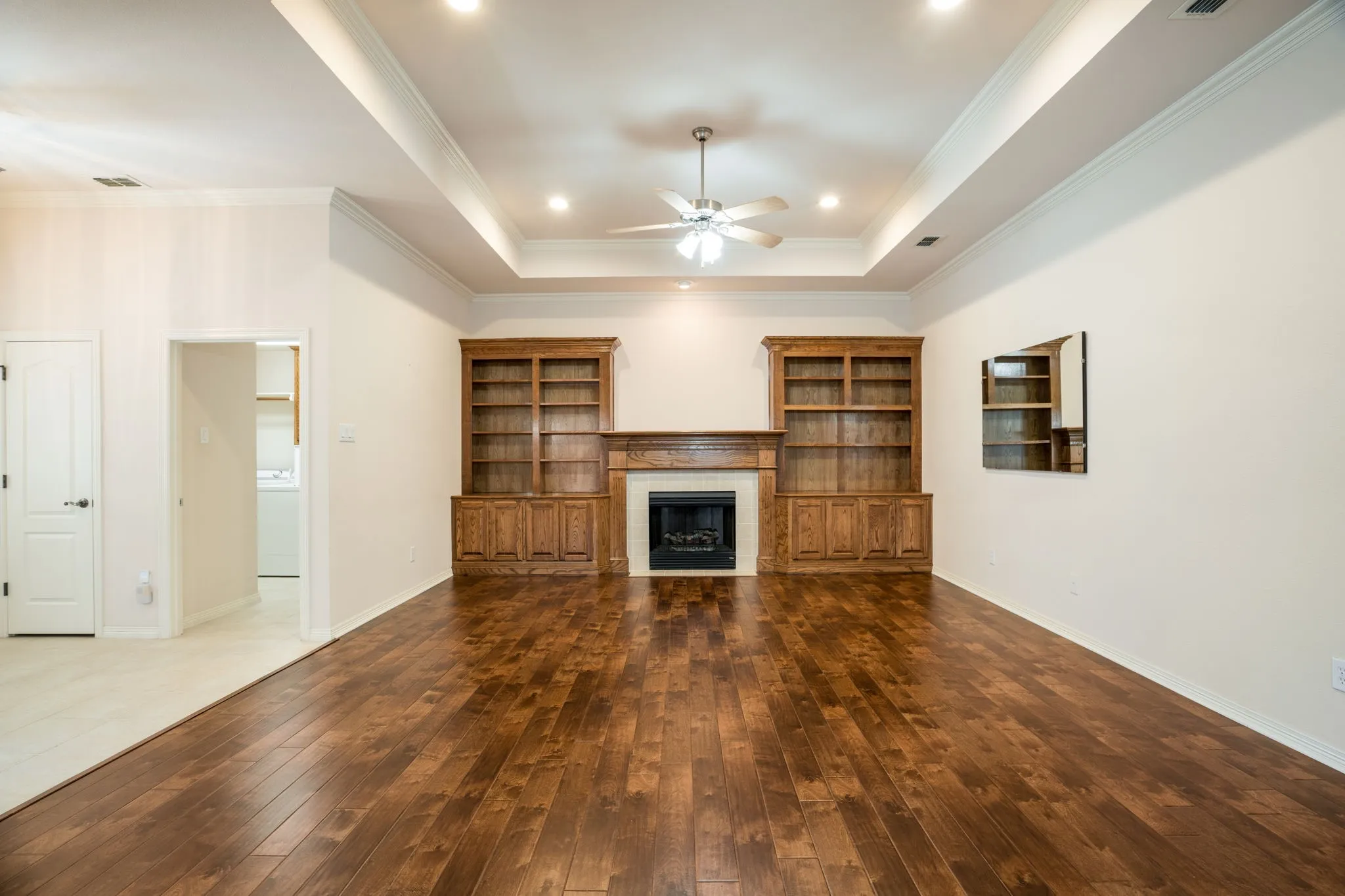 Hardwood flooring, tray ceiling, recessed lighting, built-in cabinetry, and a fireplace with a wood mantle