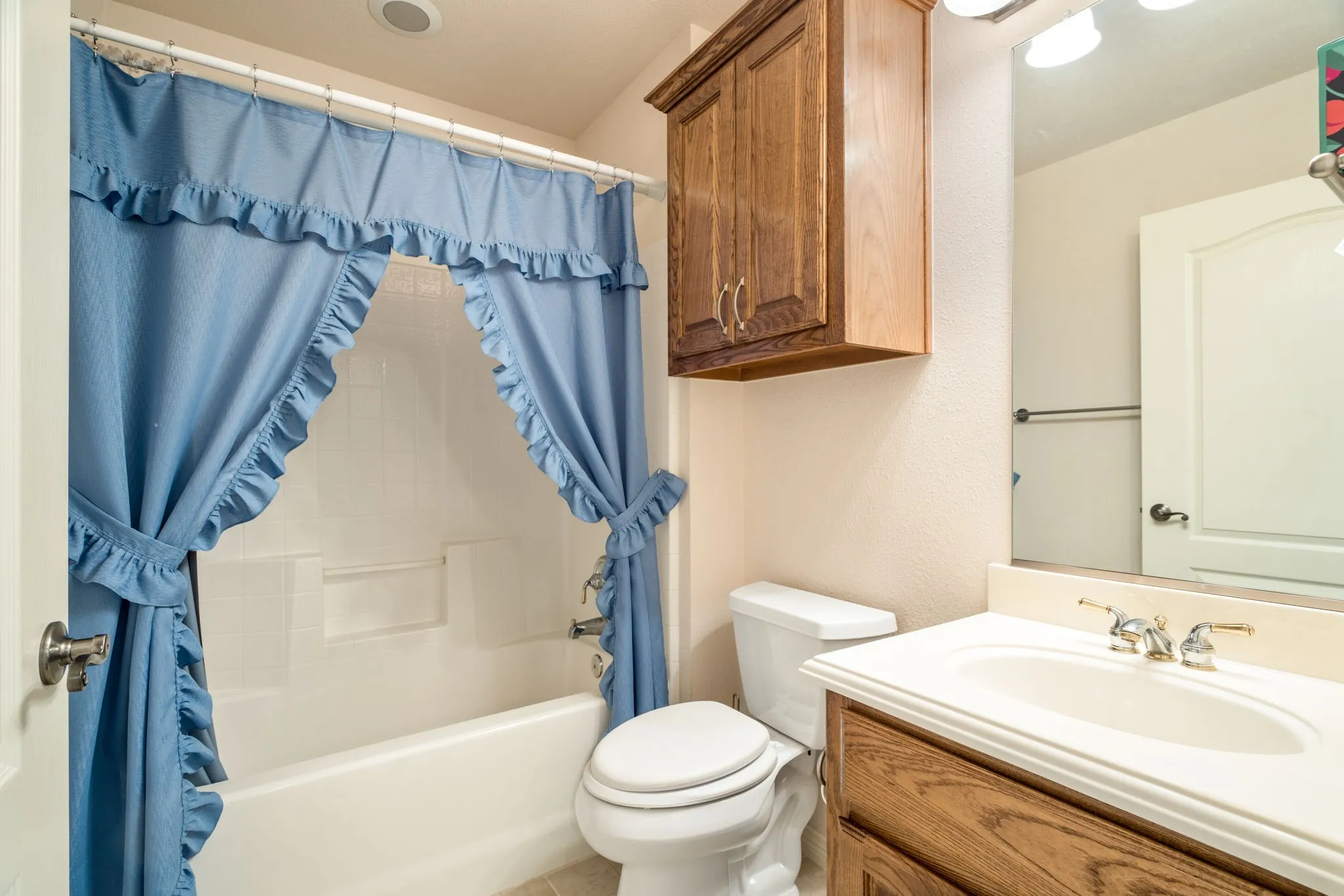 Wood-finish vanity with a white countertop sink and polished brass faucet