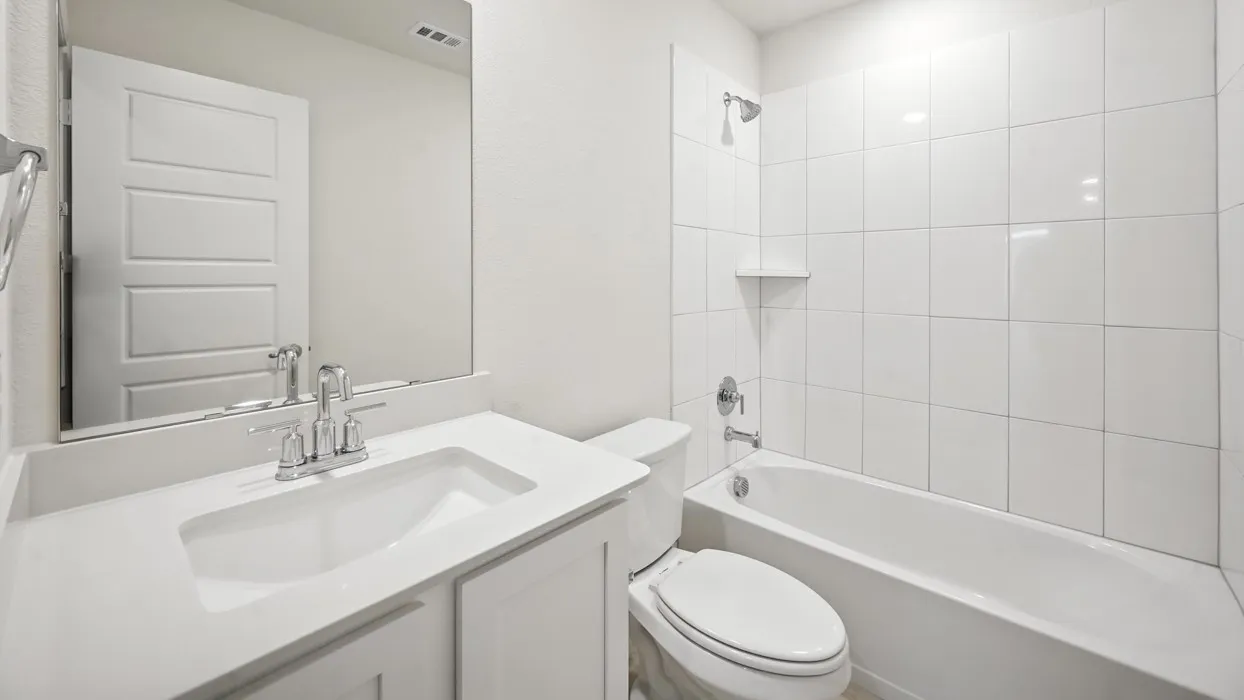 Bathroom featuring a white vanity with an integrated sink, chrome faucet, wall-mounted mirror, and a tiled shower-over-tub combination