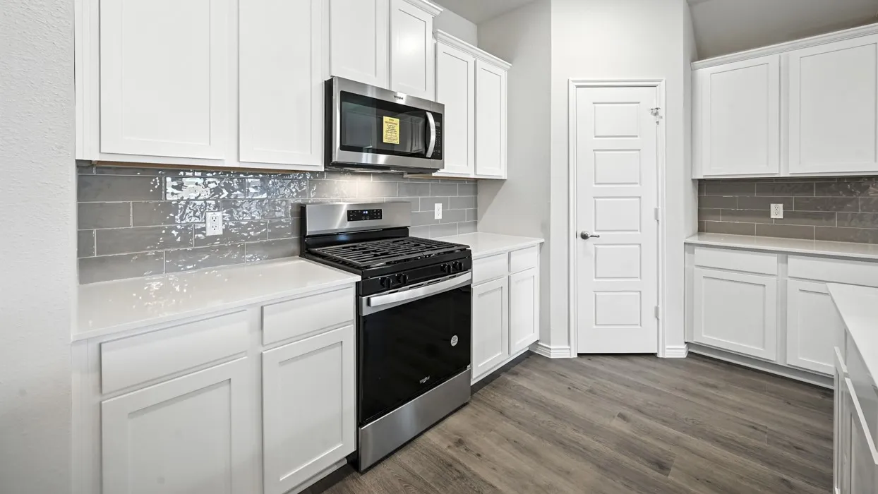 White shaker-style cabinetry, stainless steel appliances, solid surface countertops, grey subway tile backsplash, and wood-finish flooring