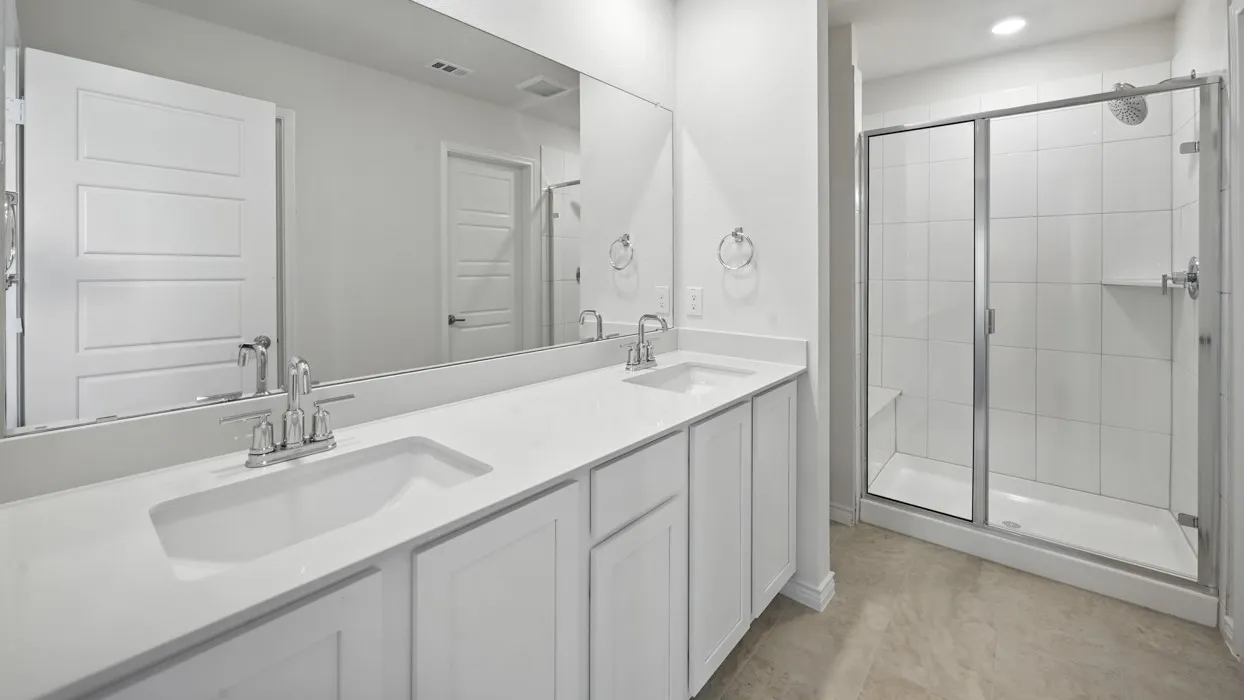 Dual vanity with undermount sinks, stone countertops, large frameless mirror, and a glass-enclosed shower with a built-in bench