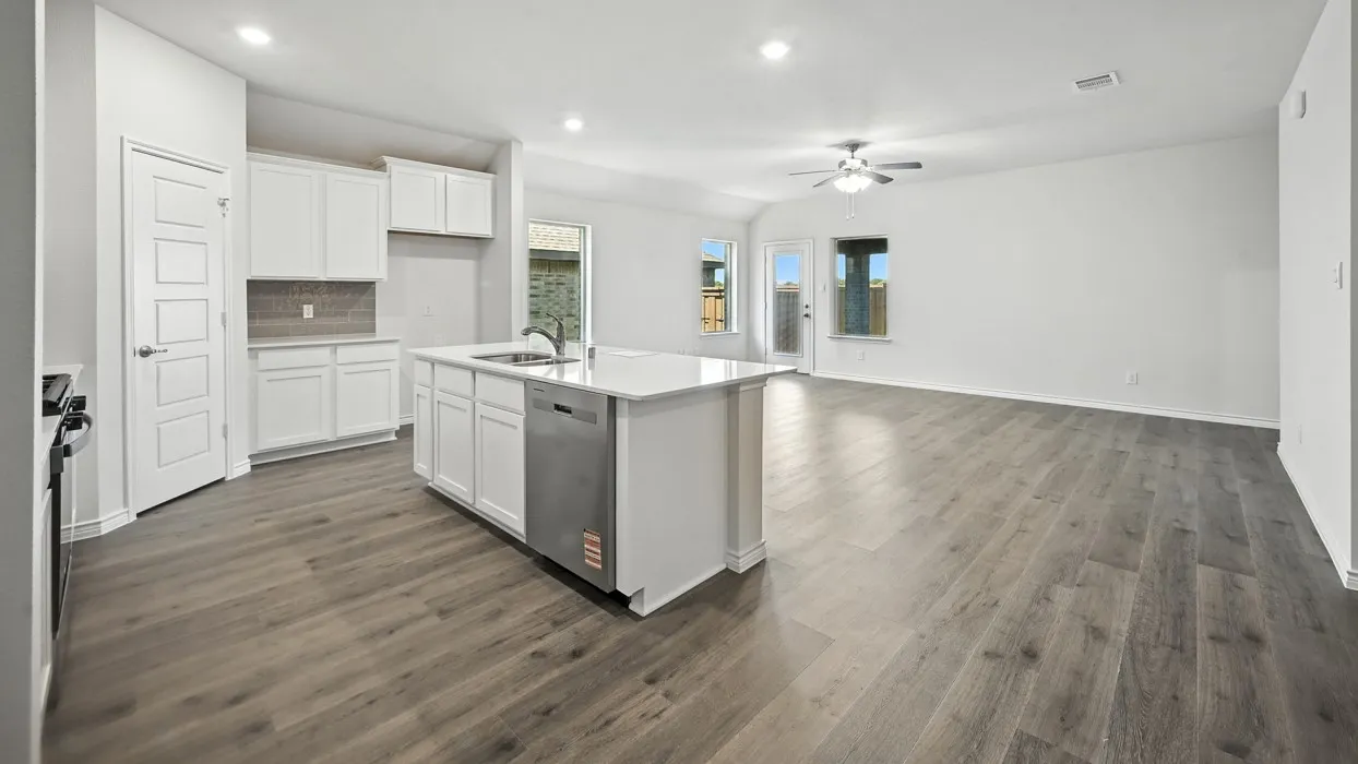 Open-concept floor plan featuring wood-finish flooring, white cabinetry, a kitchen island with an integrated sink, and stainless steel appliances