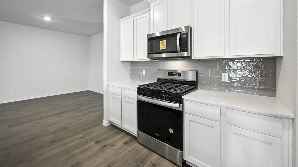 White upper and lower cabinetry, stainless steel range, stainless steel microwave, gray subway tile backsplash, and light countertops
