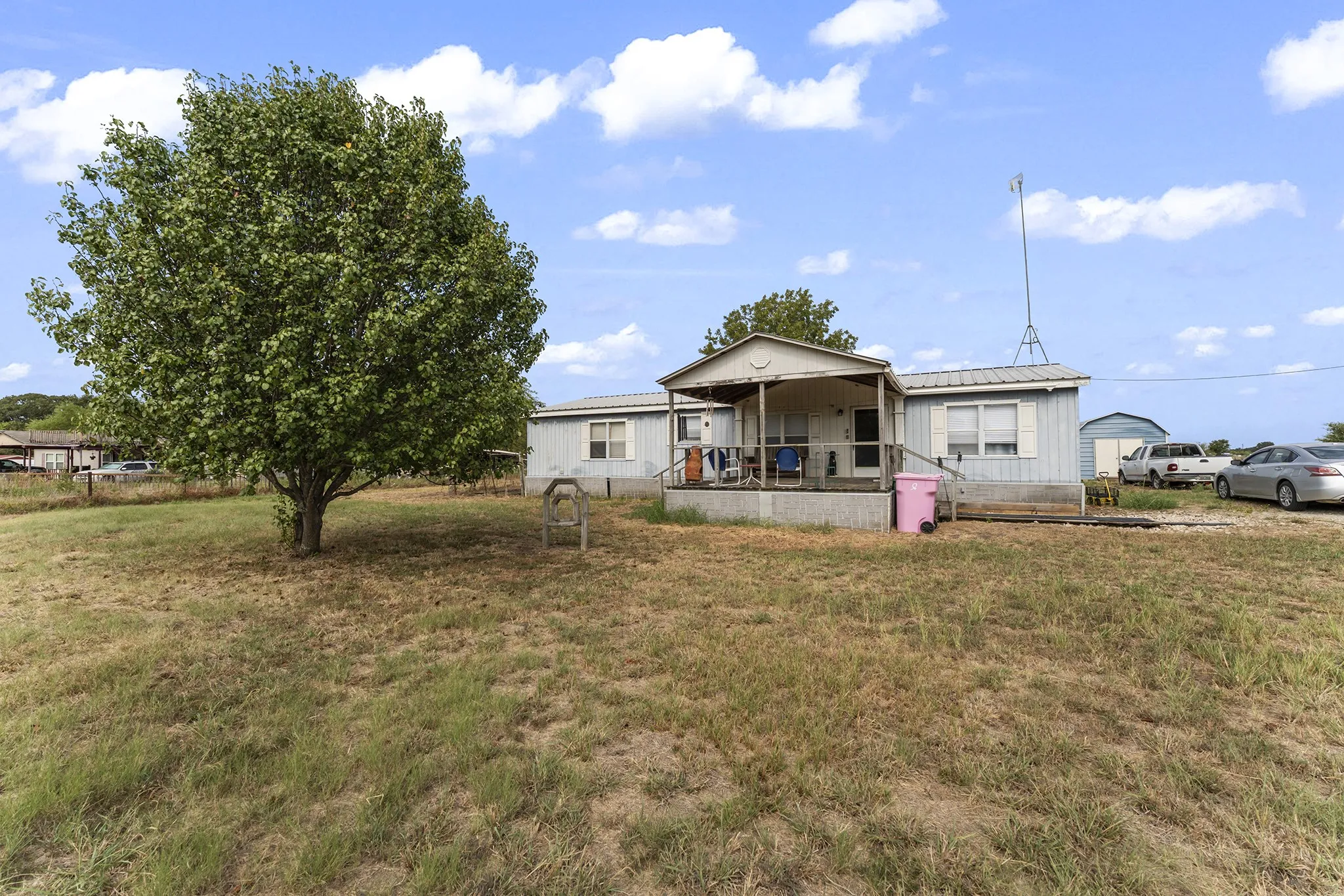 Expansive grassy lot featuring a mature shade tree, a covered porch, and a detached structure