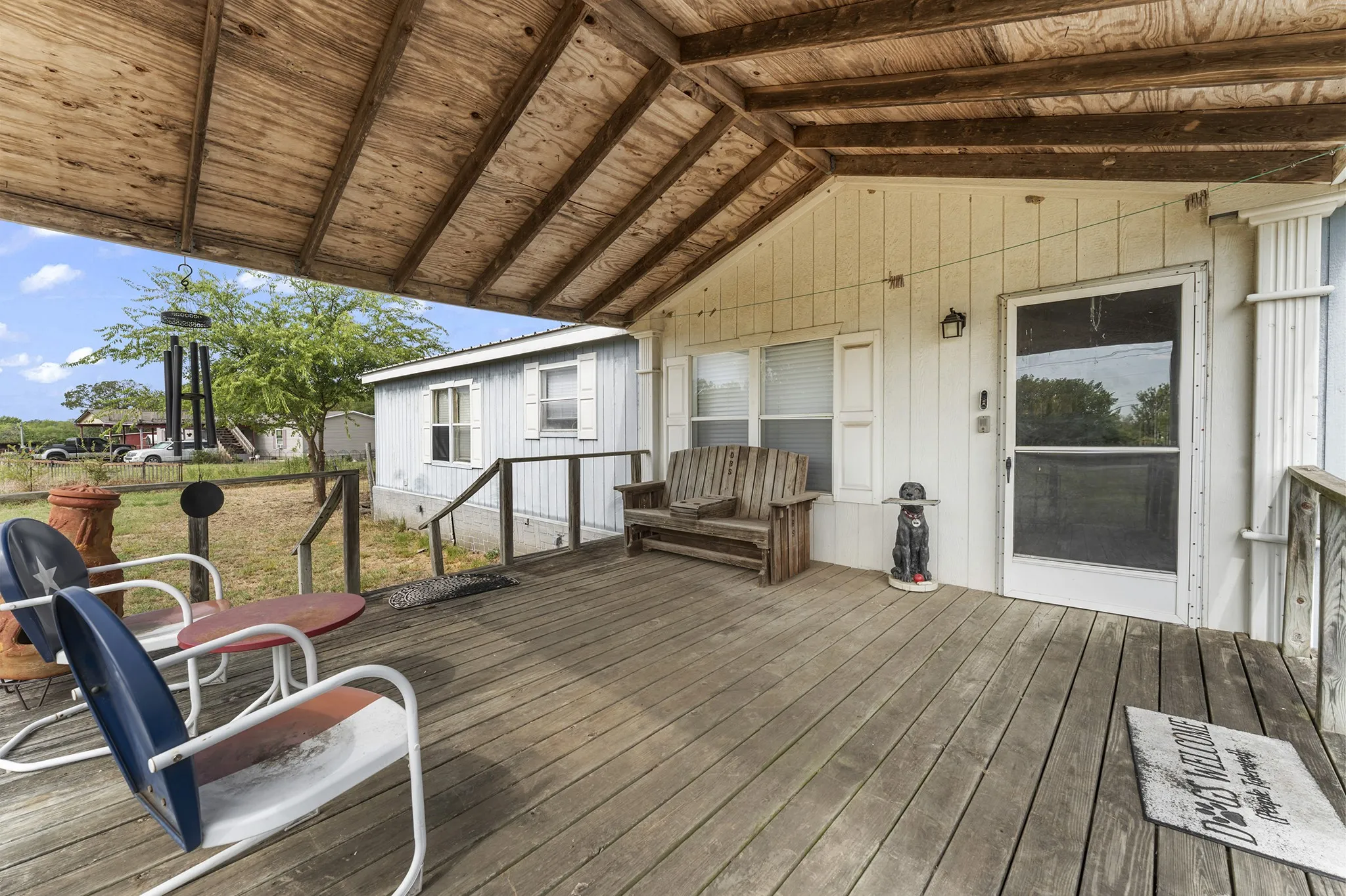 Covered wooden deck with slatted wood ceiling, white board and batten siding, and an exterior wall lantern
