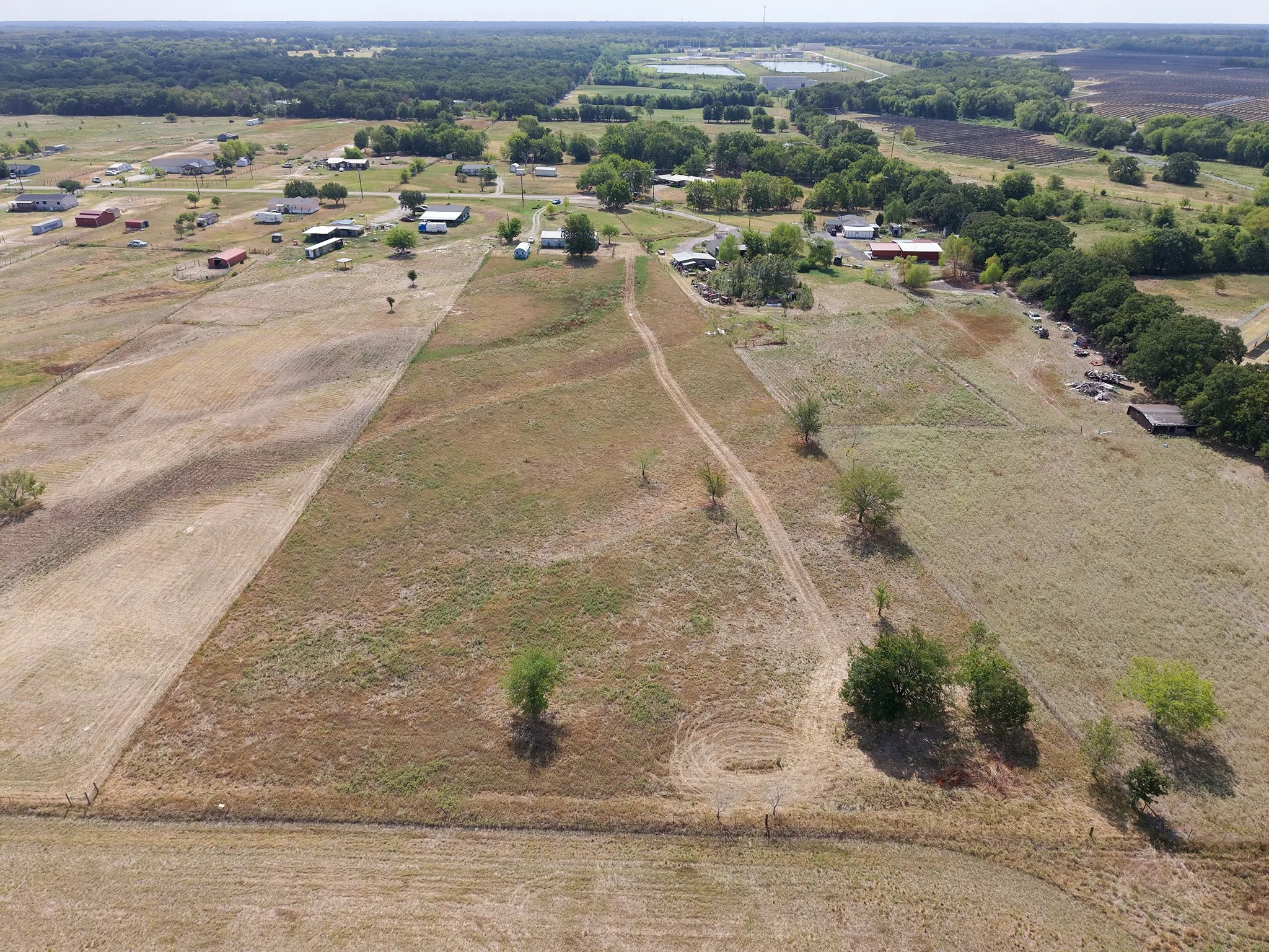 Expansive acreage with partially cleared land, scattered mature trees, and a visible unpaved track