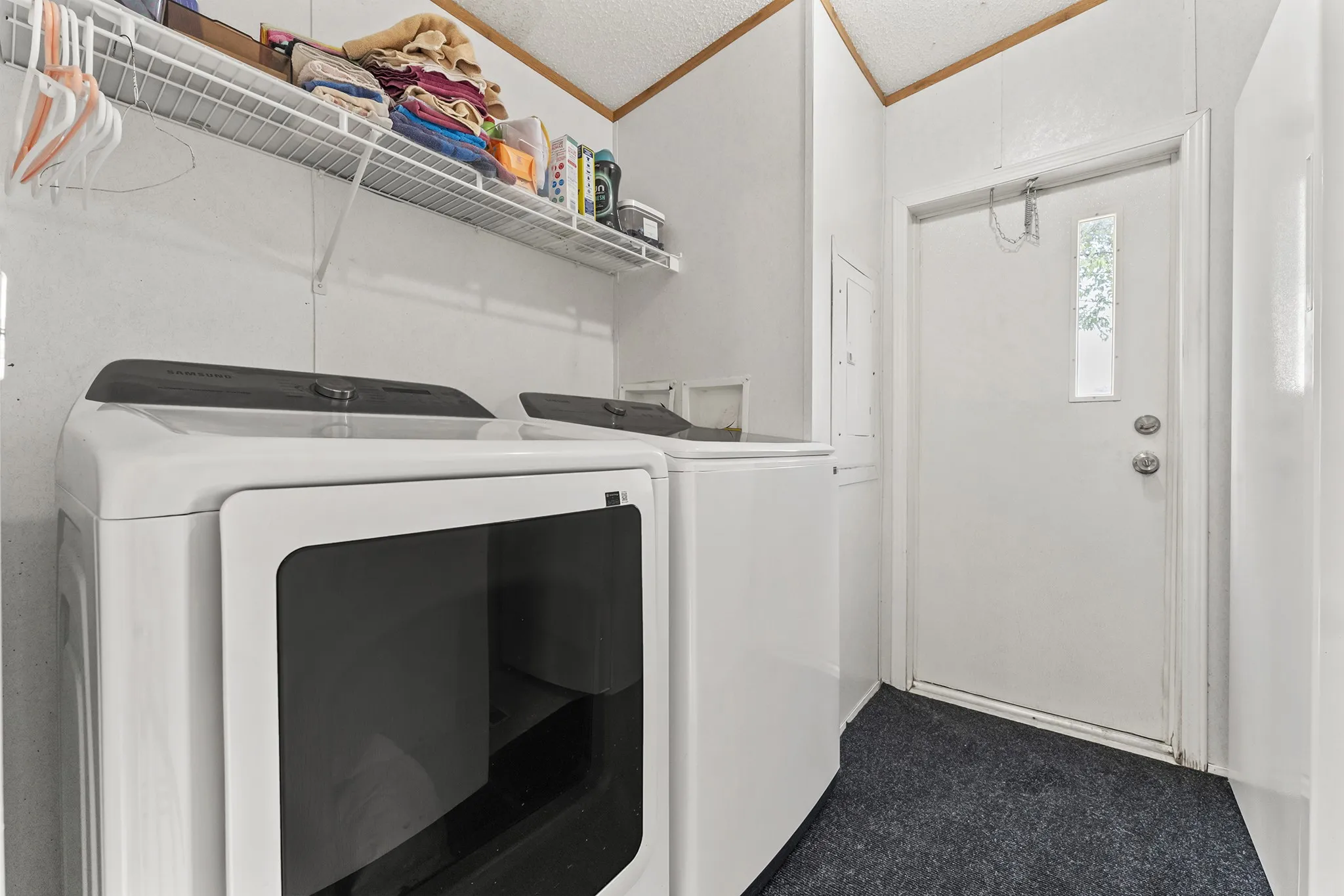Utility space featuring overhead wire shelving and a white entry door with a frosted glass insert