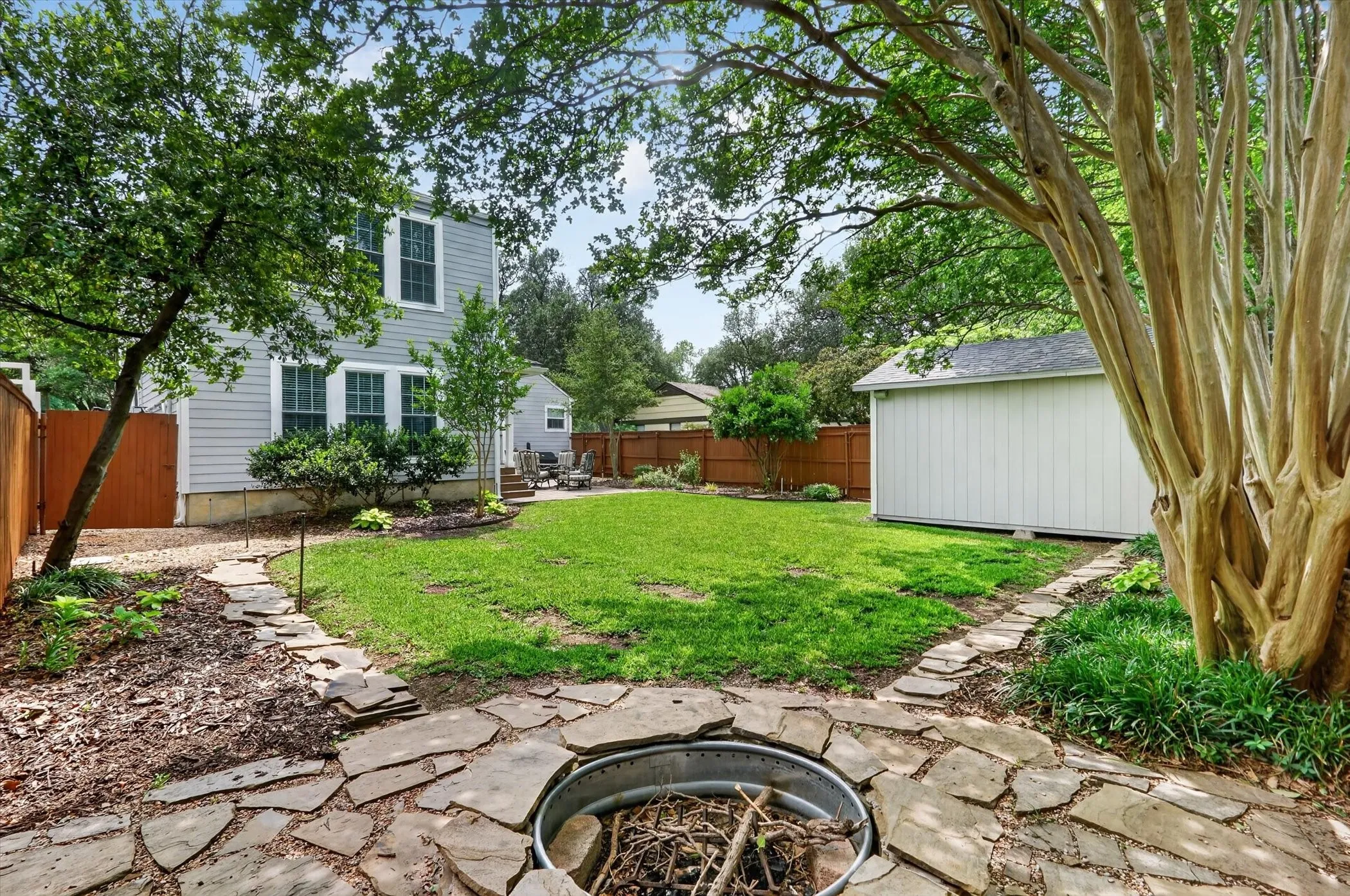 Expansive backyard featuring a central lawn, a stone fire pit, and a flagstone pathway