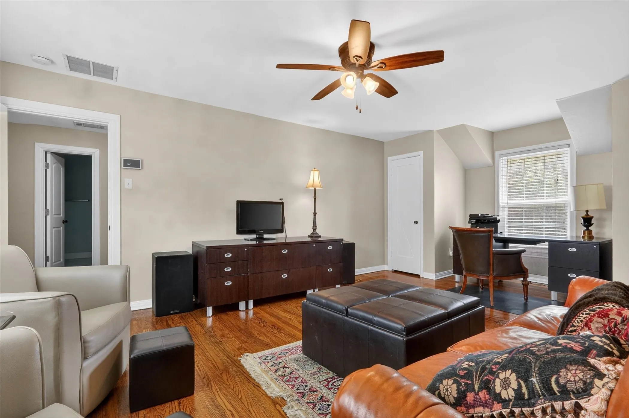 Spacious bonus room featuring wood-finish flooring, a ceiling fan with integrated lighting, a window with blinds, and neutral wall tones